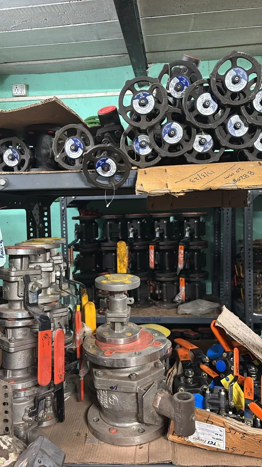 Shelf with industrial valves, regulators, and fittings in a workshop.