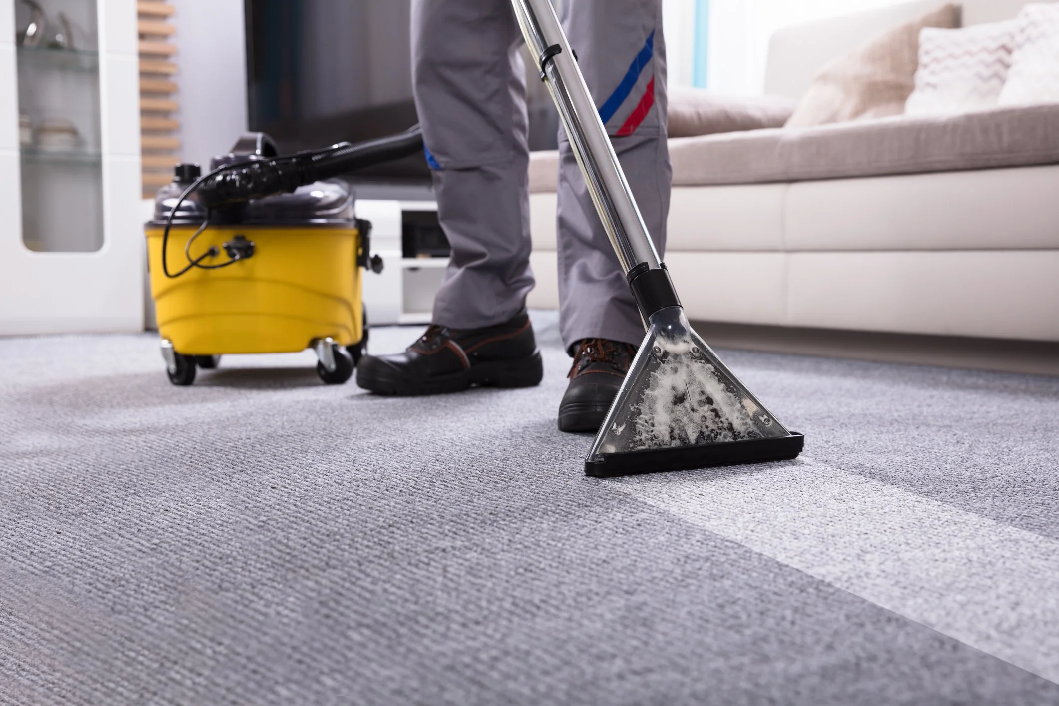 A person vacuuming a gray carpet with a yellow and black vacuum cleaner in a living room.
