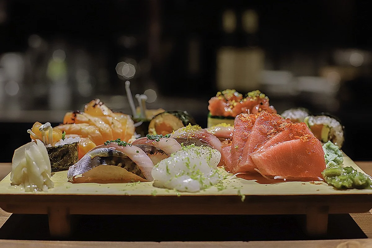 Plato de sashimi y sushi con diferentes tipos de pescado y mariscos, acompañado de salsa y otros ingredientes