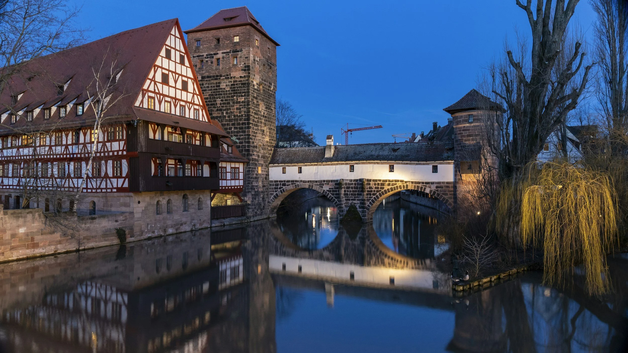 Nürnberg: Historische Brücke über einen Fluss, umgeben von alten Gebäuden und Bäumen bei Abenddämmerung.