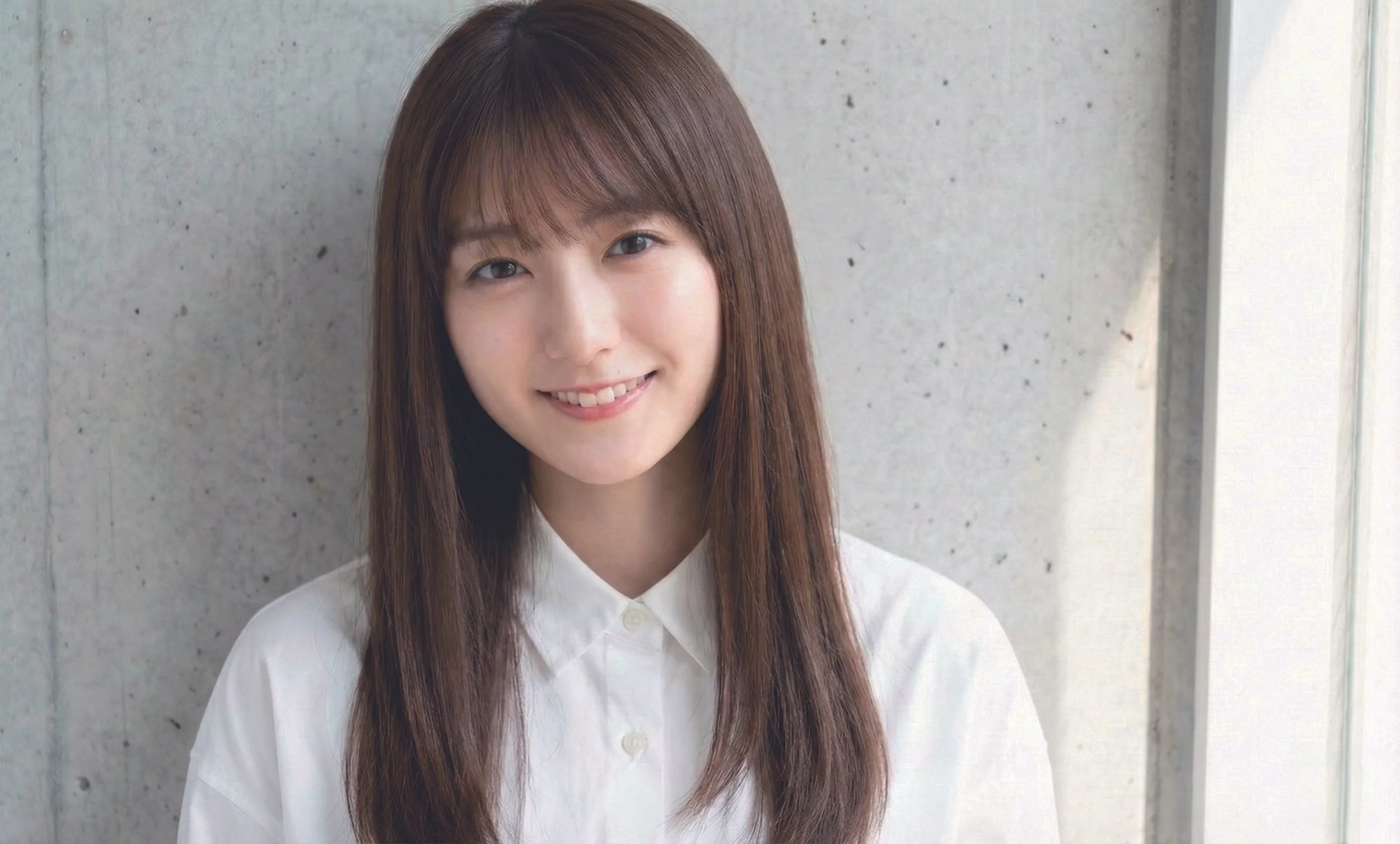 笑顔の若い女性が壁の前に立っている肖像写真