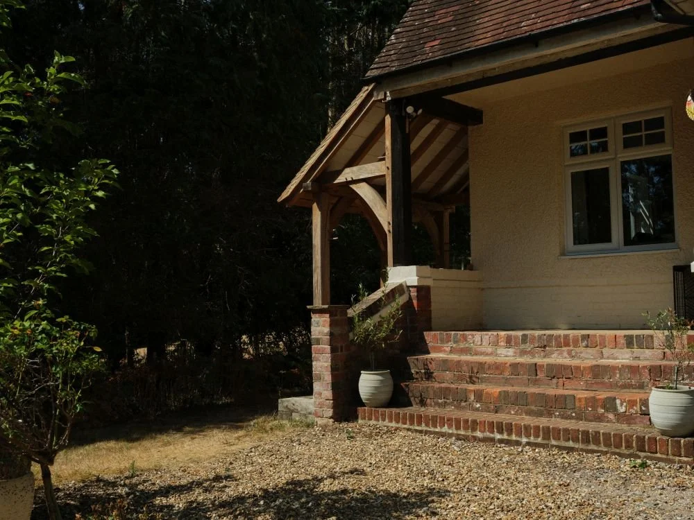 A house with brick steps leading up to the front porch, with potted plants on either side, surrounded by greenery and trees.