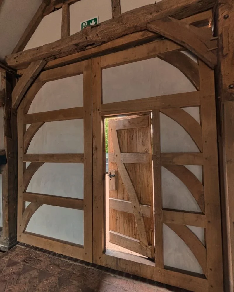 A rustic, wooden barn-style door set into a wall with a small opening at the top, featuring diagonal bracing and decorative curved wood supports.