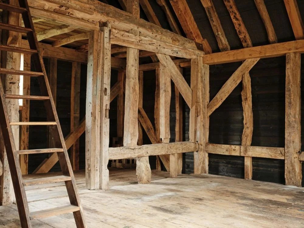 Interior of a wooden building under construction with exposed wooden beams, a ladder, and a loft area.