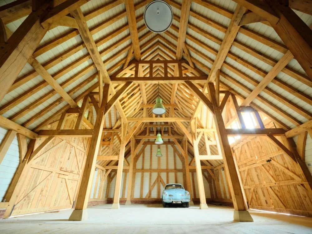 A large, empty wooden barn with a vintage white car parked inside.