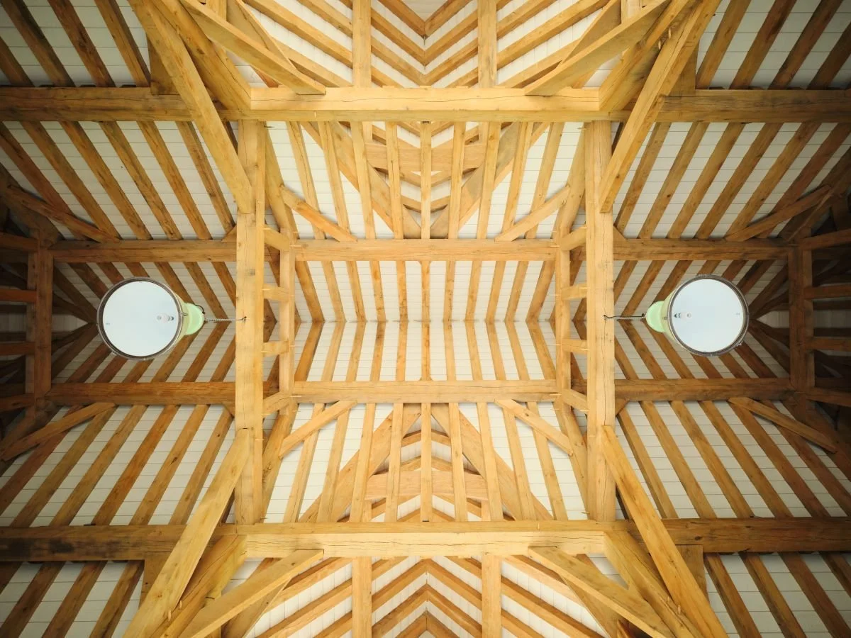 Ceiling of a wooden structure with exposed beams and two hanging white lights.