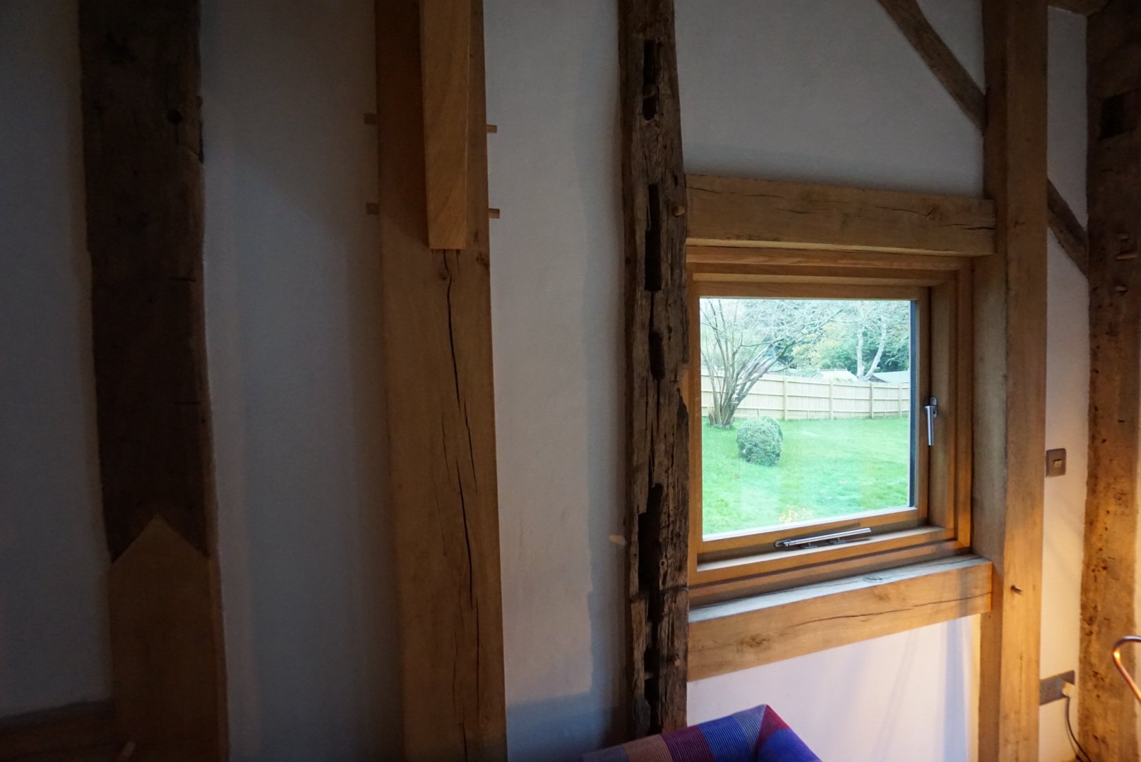 A window with wooden trim in a room, showing a grassy yard with trees and a wooden fence outside.