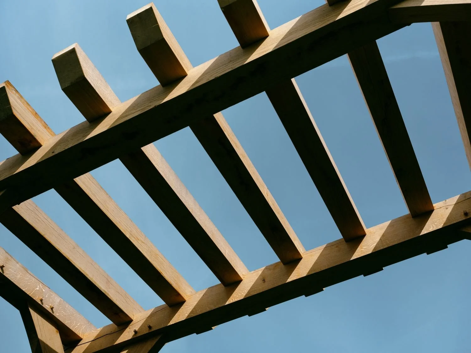 Close-up of a wooden pergola with beams and slats against a clear blue sky.