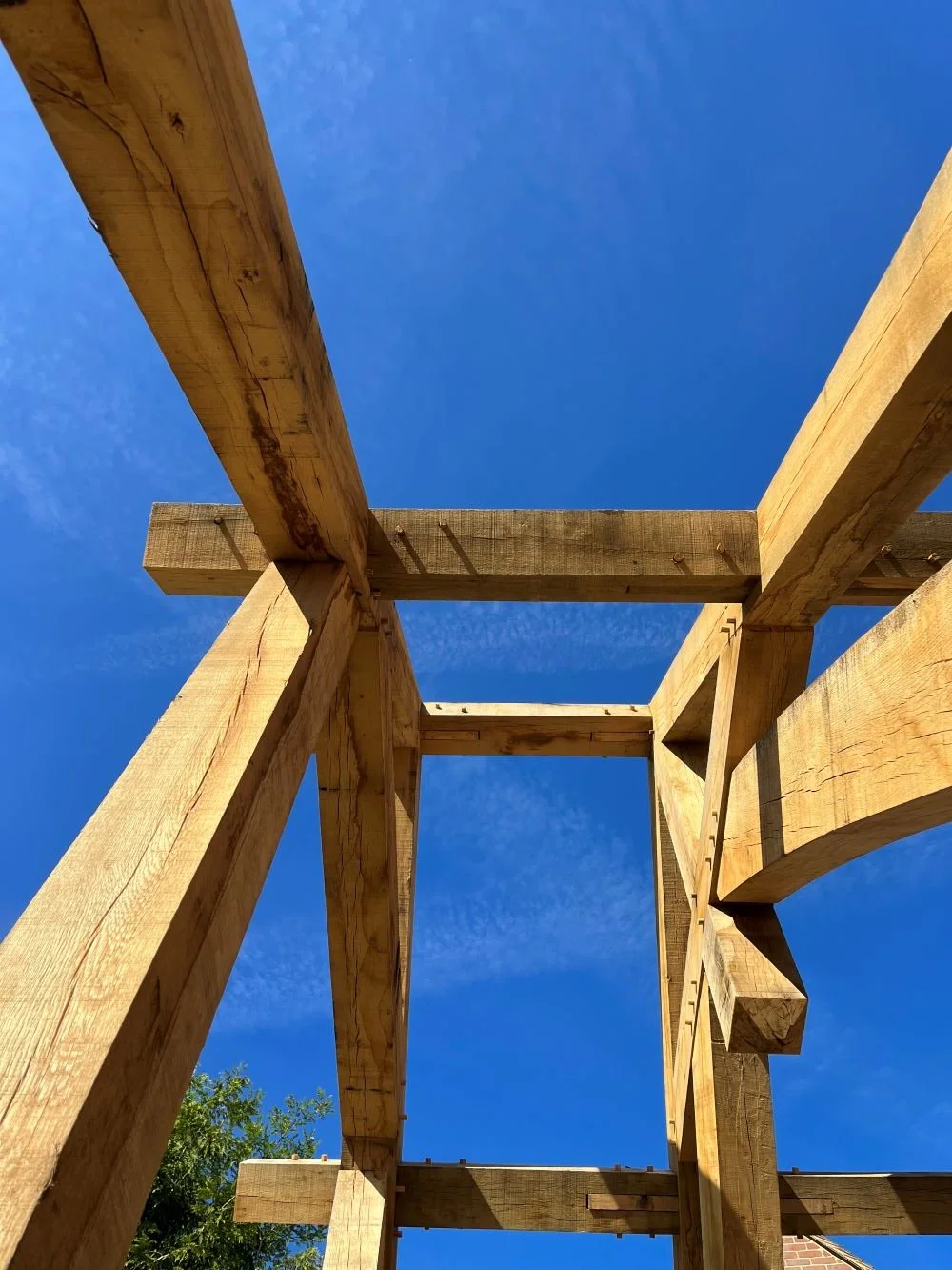 View of a wooden structure under construction with beams against a bright blue sky.