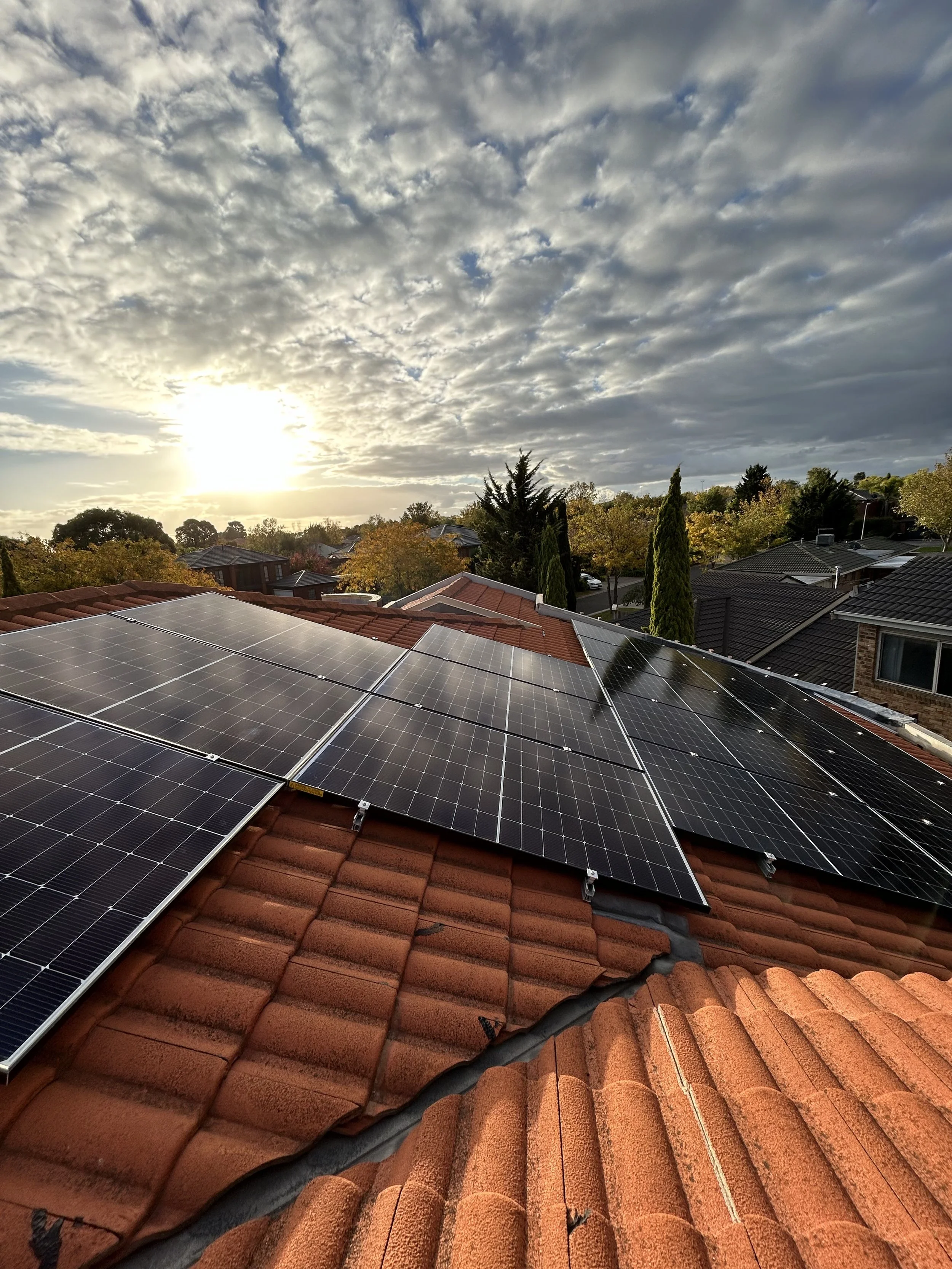 Residential roof with solar panels, orange tiles, and a partly cloudy sky during sunset.