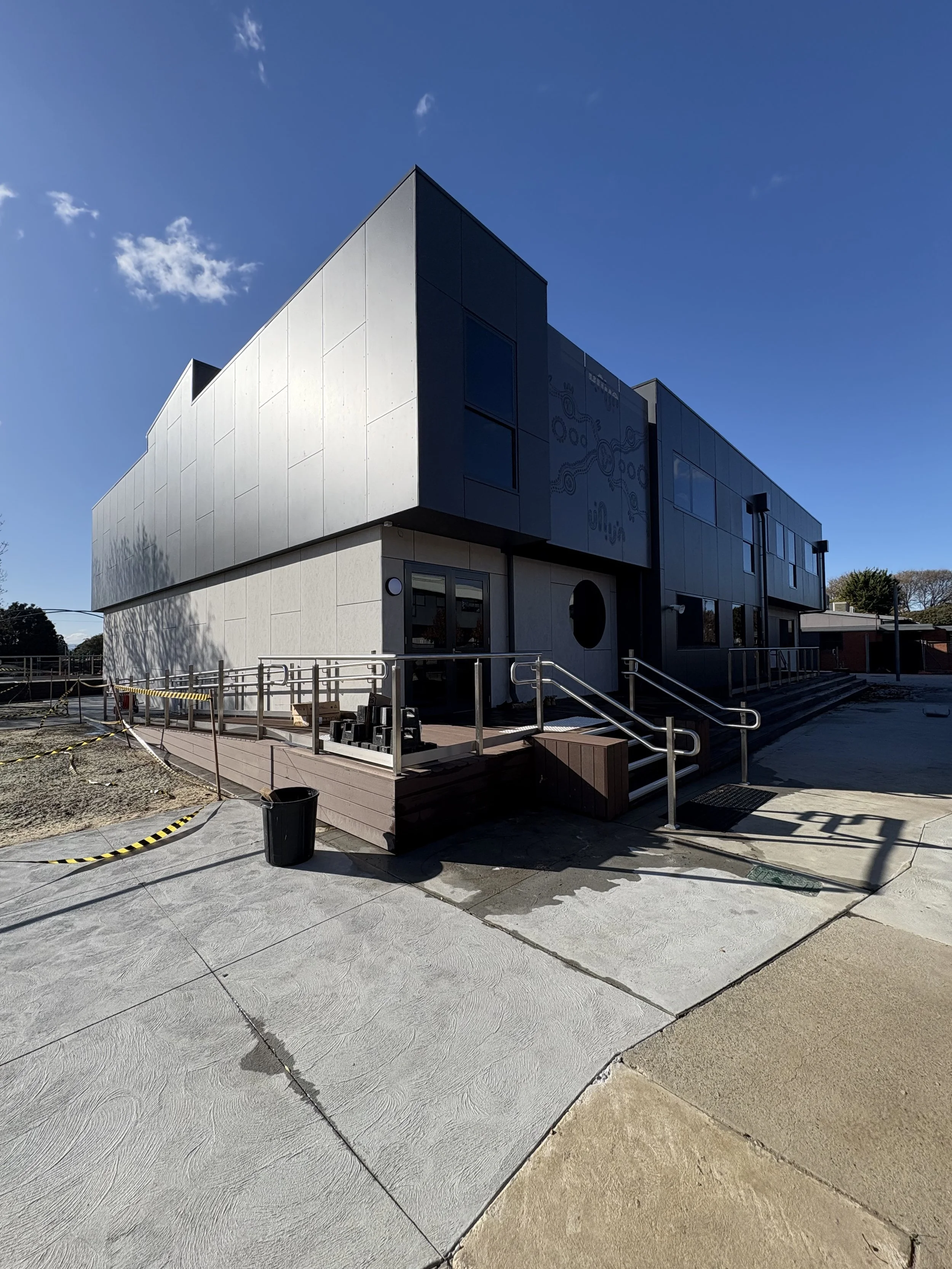 Modern two-story building with black and white exterior, with stairs and ramps leading to the entrance, and a partly cloudy blue sky in the background.