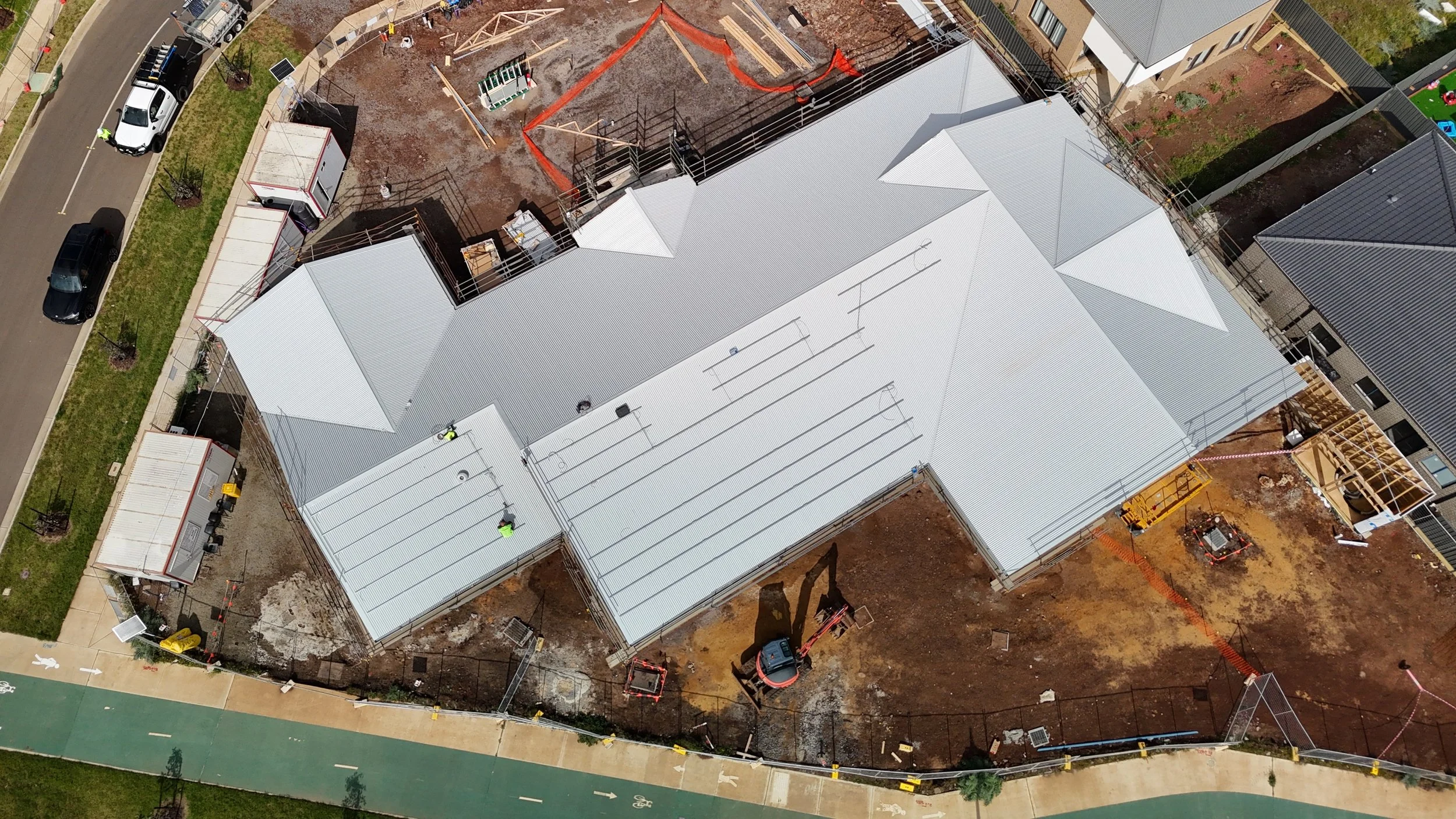 Aerial view of a house under construction with a metal roof, construction workers, and construction equipment on the site.