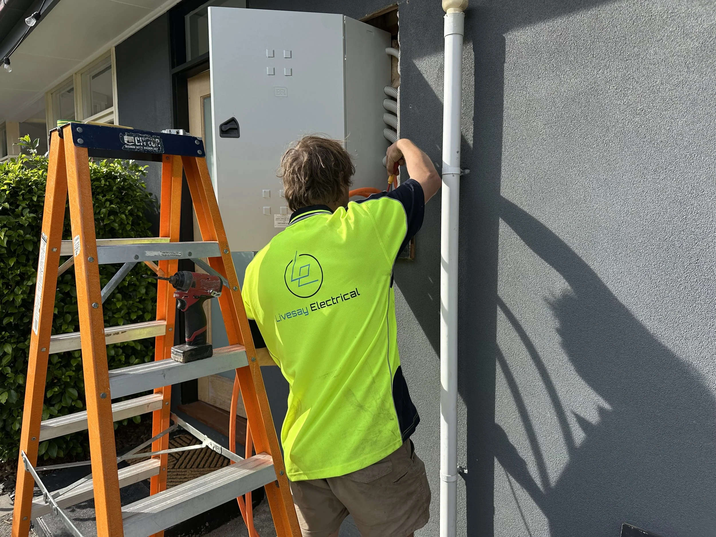 Electrician working on a switchboard with the logo for Livesay Electrical on his yellow work shirt