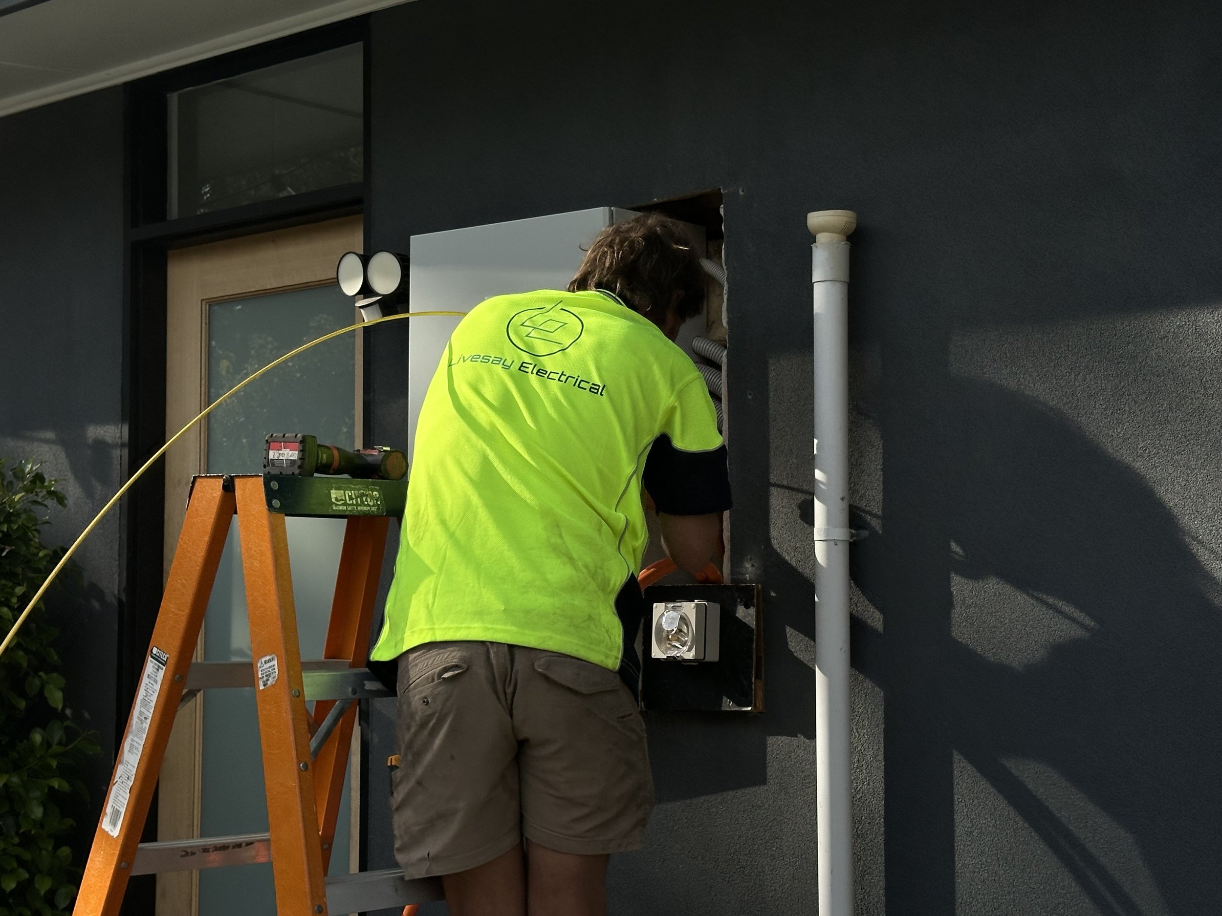 An electrician with Livesay Electrical shirt working on a switchboard