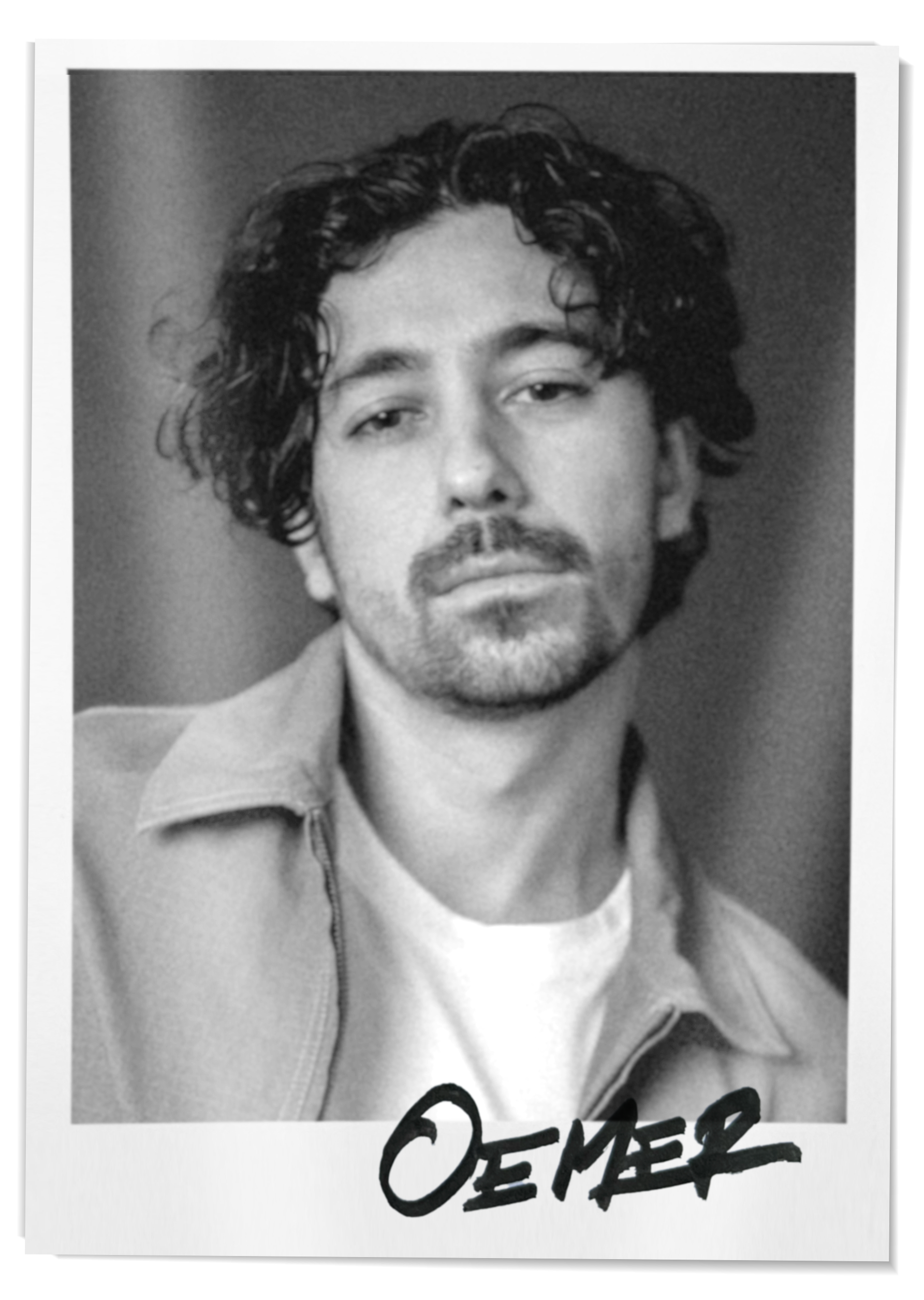 Schwarz-weiß-Fotografie eines Mannes mit länglichem, lockigem Haar und Bart, trägt eine Jacke und ein T-Shirt, mit einem unterschriebenen Namen am unteren Rand.