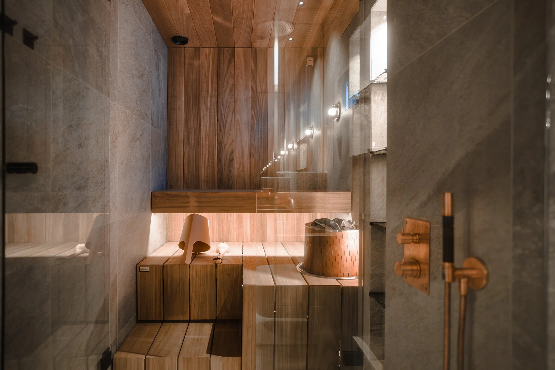 A modern spa room with wood and stone elements, a sauna, and a copper bathtub.