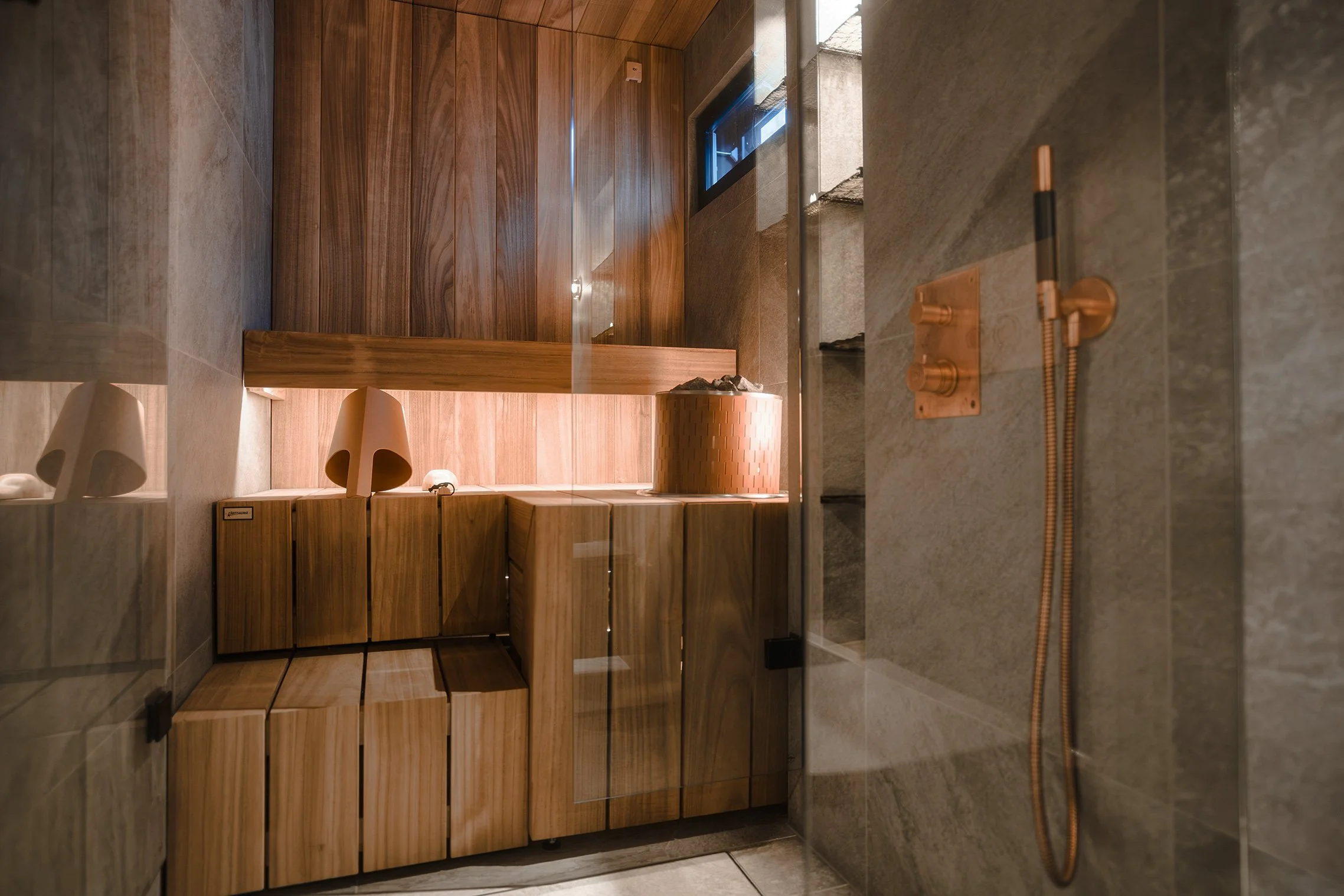 Modern bathroom with wood cabinetry, a shower area with a copper-colored handheld showerhead, and stone wall tiles.