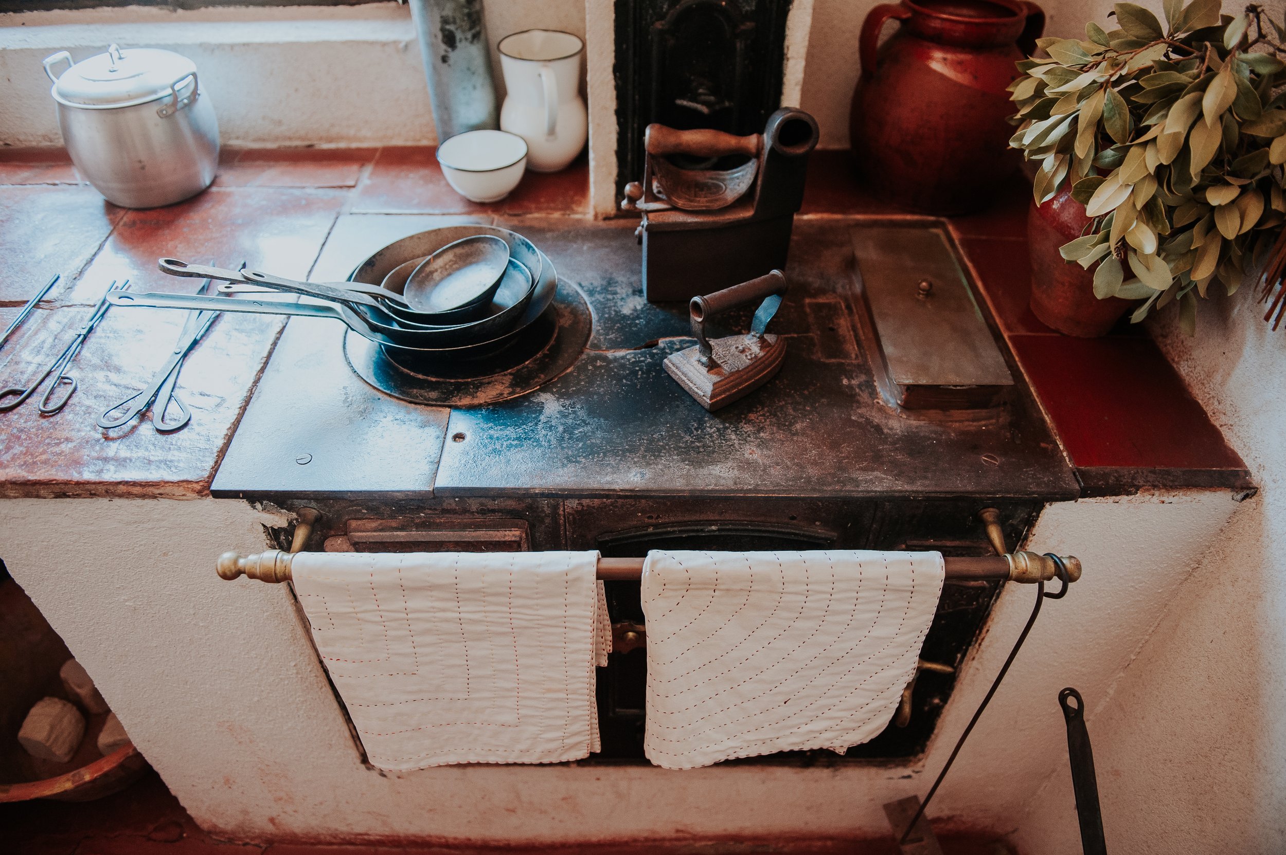 Estufa antigua de hierro con utensilios de cocina de metal, tazas, jarrones y plantas decorativas en una cocina tradicional