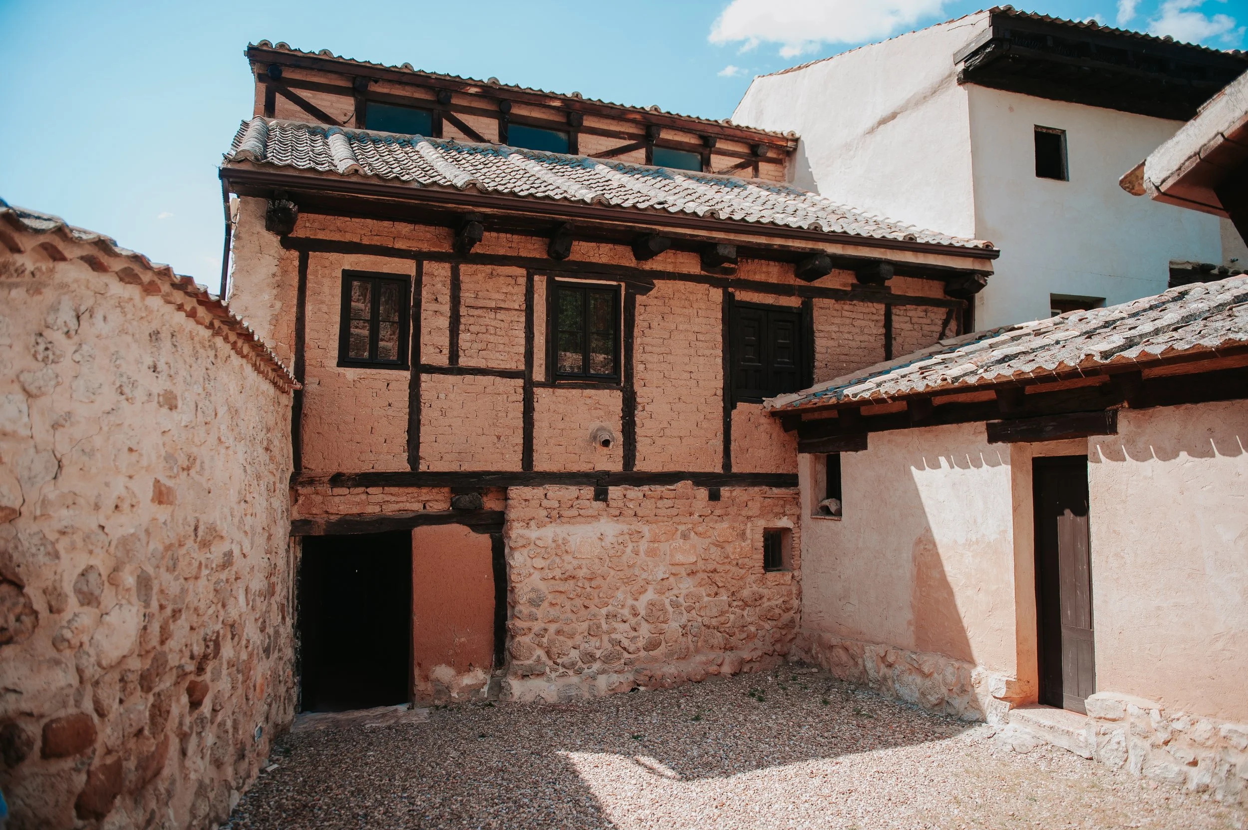 Edificio antiguo de ladrillos y madera, con tejado de tejas y puertas y ventanas en una calle de piedra, en un día soleado con cielo azul.