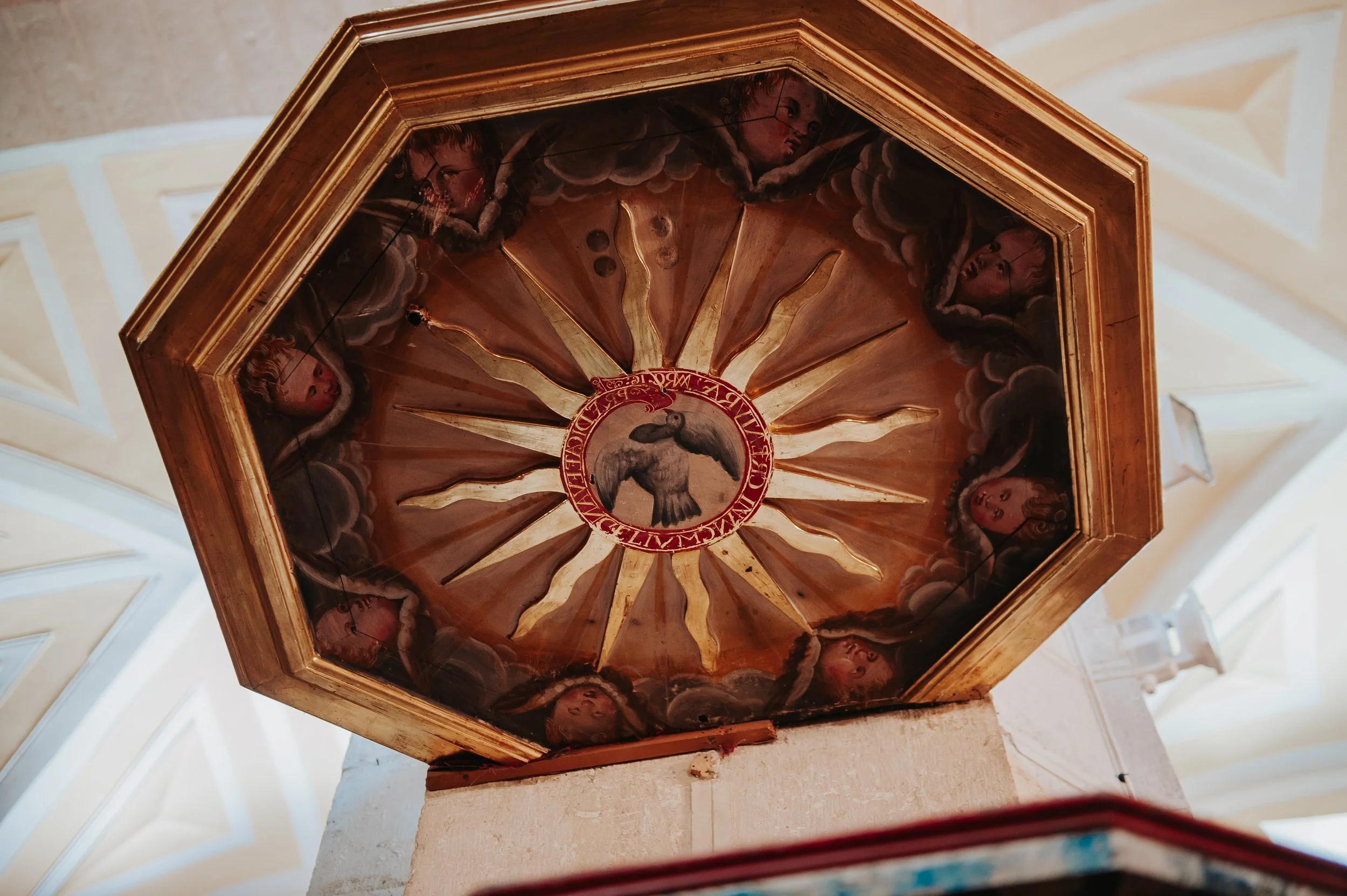 Techo decorado con pintura de ángeles y una paloma en el centro, rodeada de un marco de madera y detalles dorados.