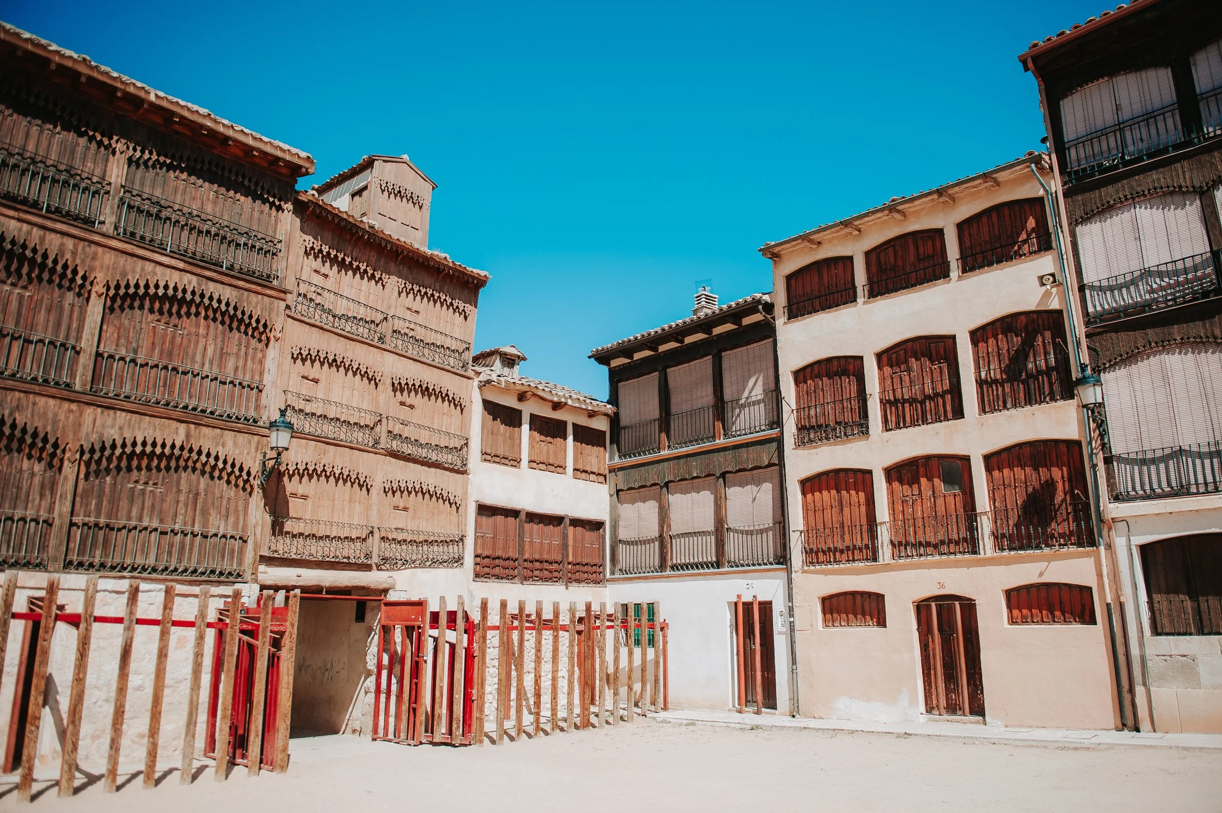 Edificios de madera y piedra con balcones y ventanas, bajo un cielo azul, en una calle vacía.