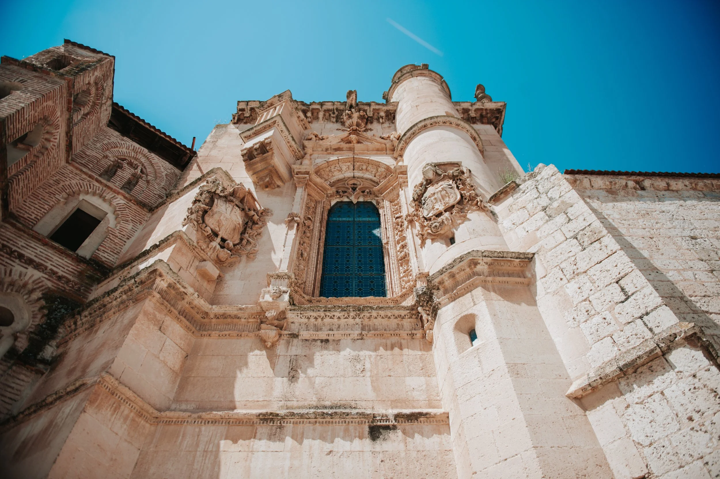 Vista aérea de una iglesia o catedral de estilo colonial con detalles ornamentales en la fachada, paredes de piedra y ventanas con vitrales, contra un cielo despejado de color azul.