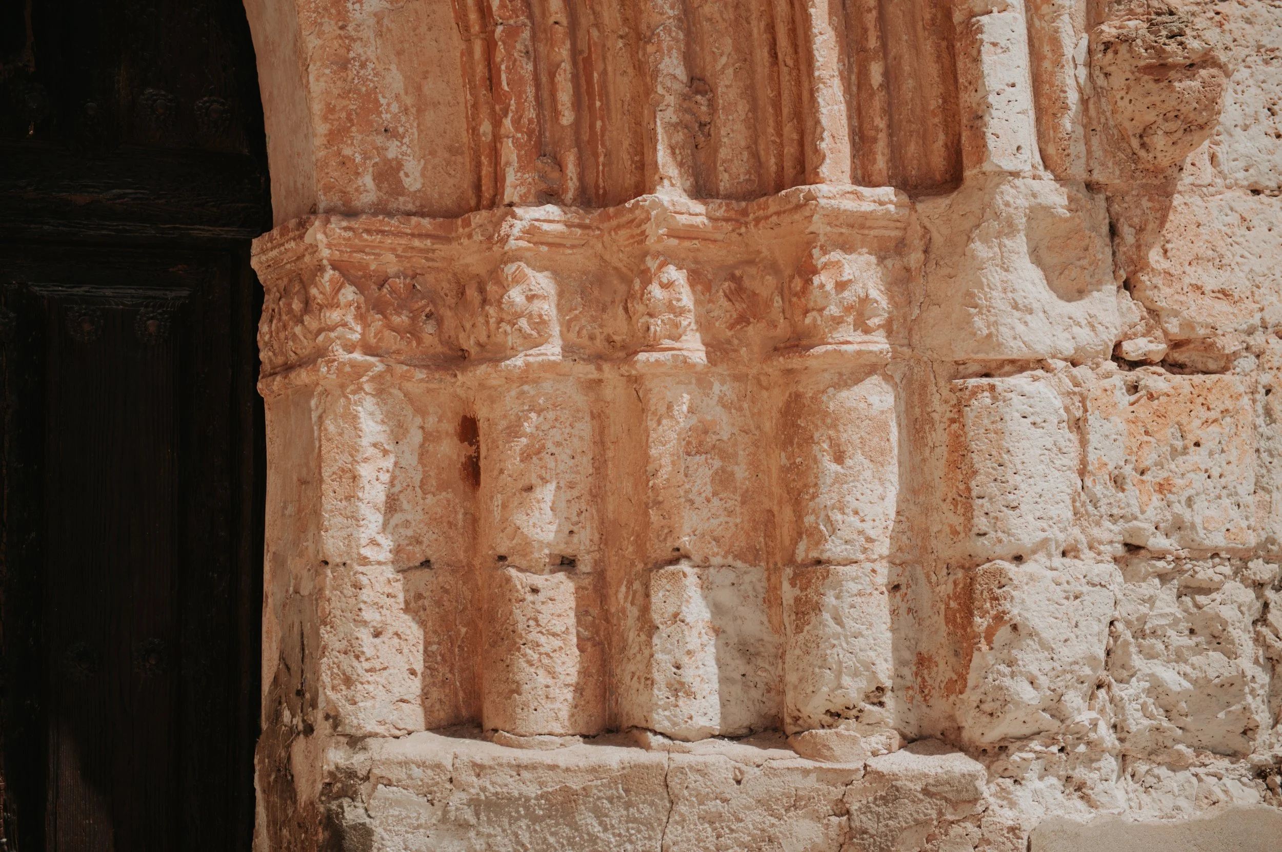 Pared de piedra antigua con detalles decorativos y puerta de madera oscura.