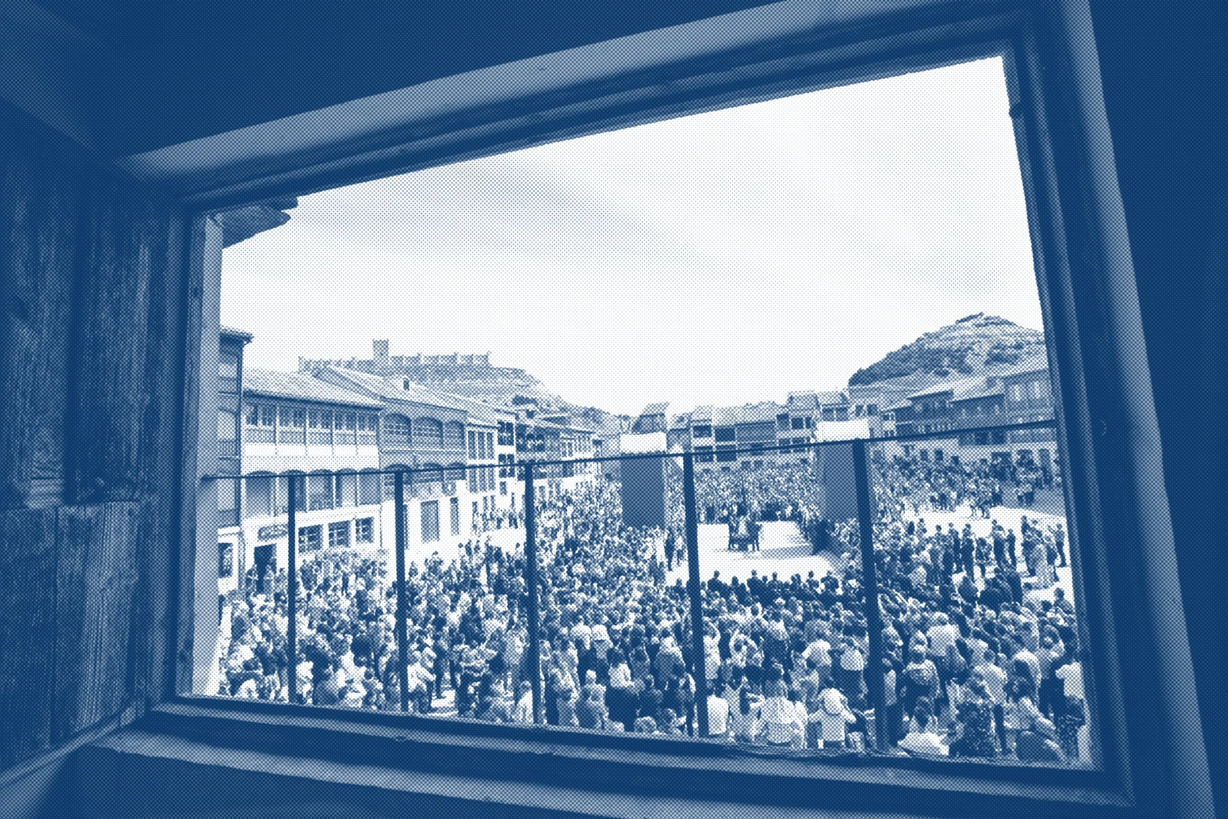Vista de una multitud de personas en un patio escolar visto desde una ventana.