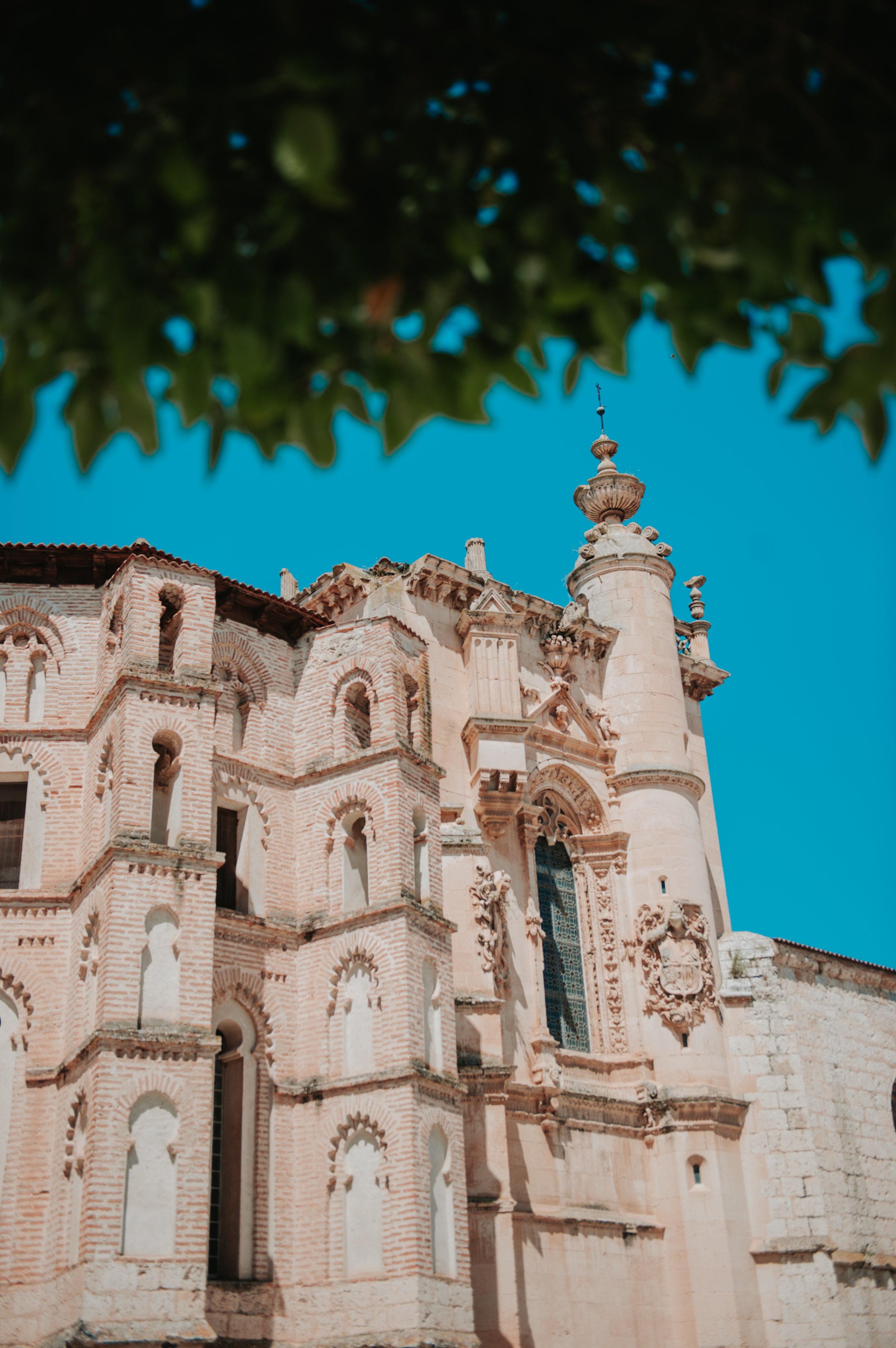 Vista de una iglesia con arquitectura barroca y detalles decorativos, con un cielo azul de fondo y hojas verdes en la parte superior.