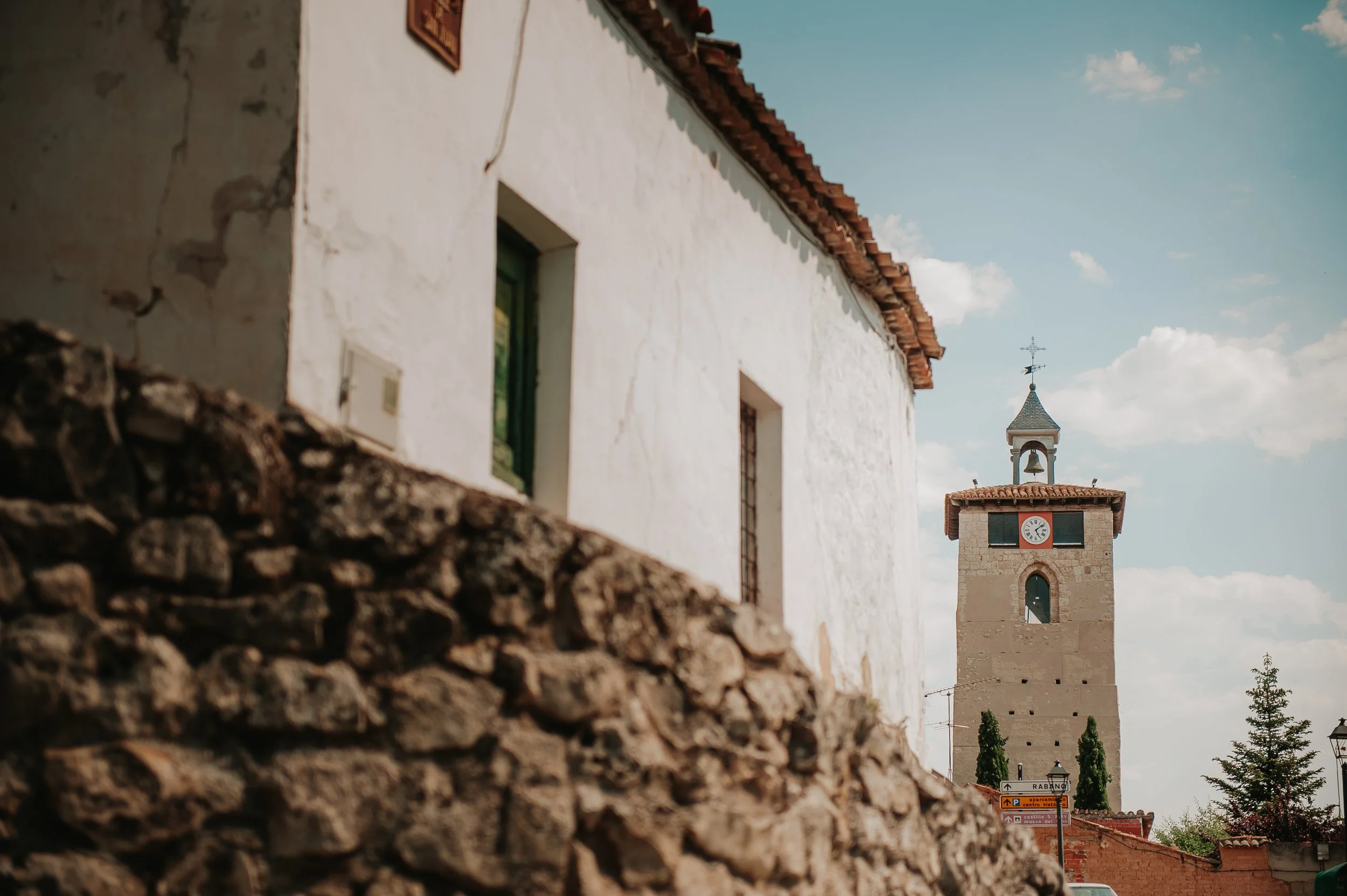 Vista de una iglesia con reloj y campana, al fondo el cielo con nubes y árboles cerca