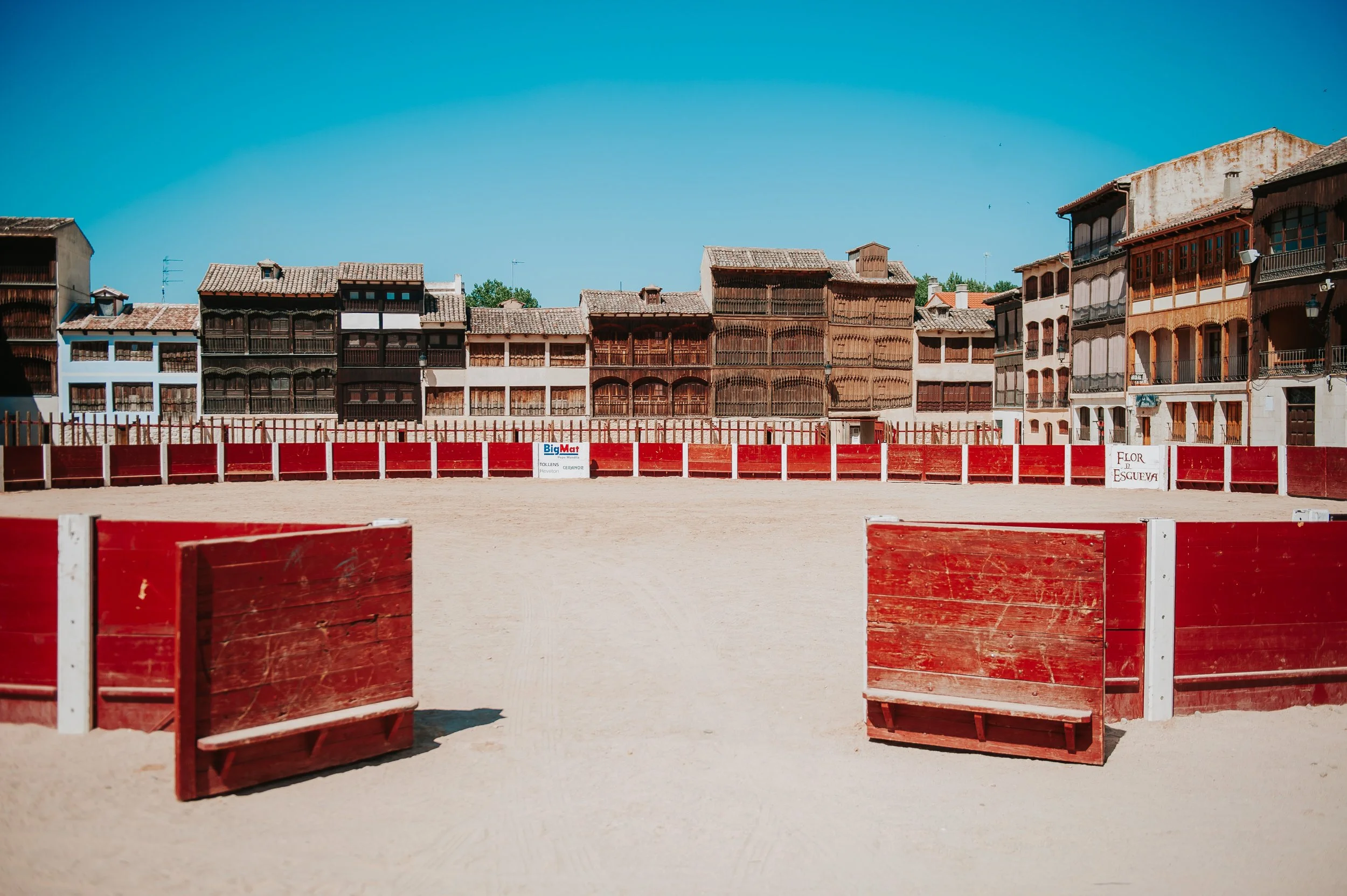 Plaza de toros vacía con barreras rojas y edificios antiguos de madera al fondo