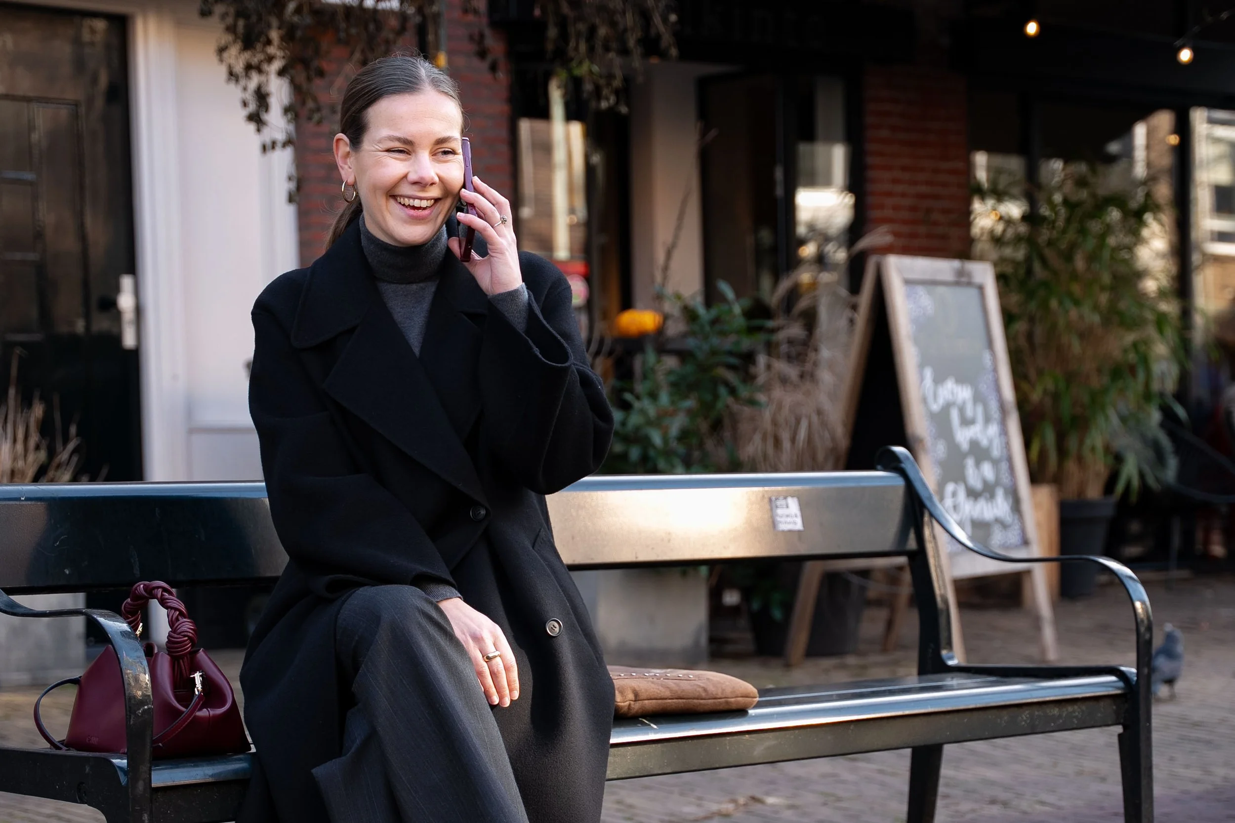 Medewerker Eva Deutekom buiten op bank aan de telefoon tijdens bedrijfsfoto's EyeCare door Studio Brenda bedrijfsfotografie