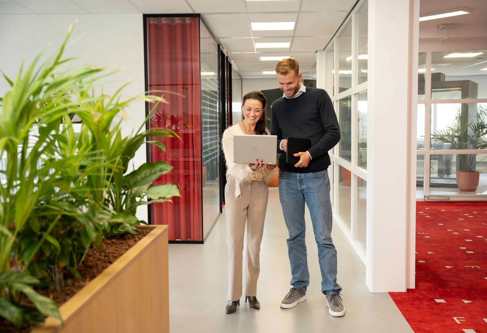 Twee mensen in een kantoor die samen naar een laptop kijken en lachen.