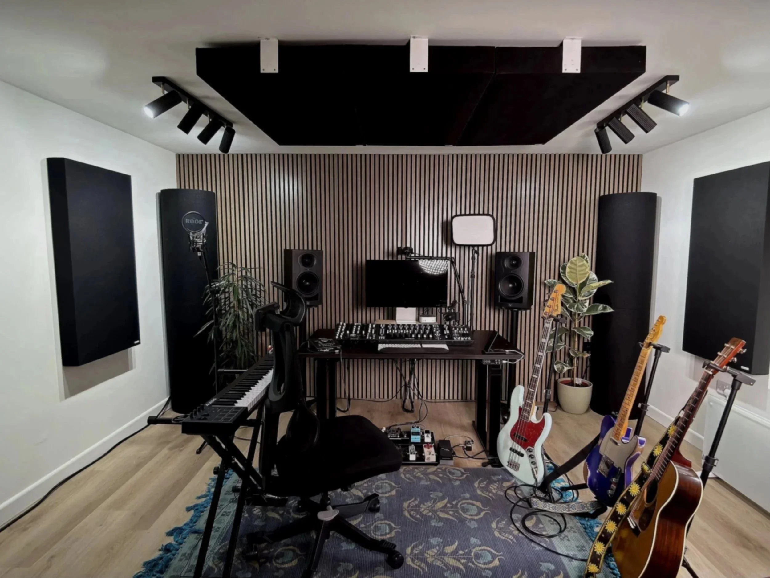 Music studio with guitars, keyboard, sound equipment, and acoustic panels.