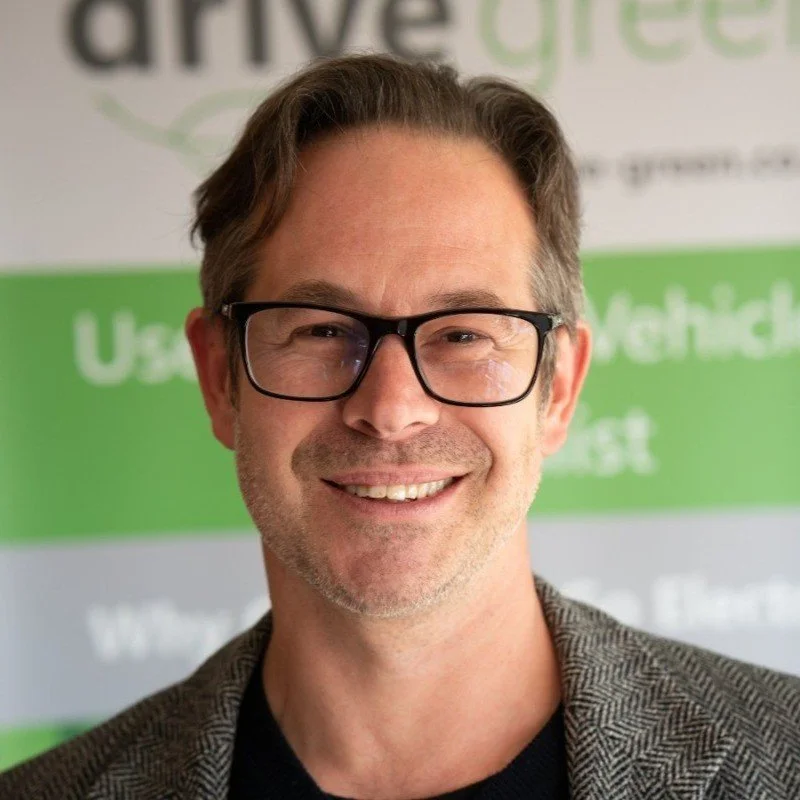 Smiling man with glasses in front of a green and white background with partial text.