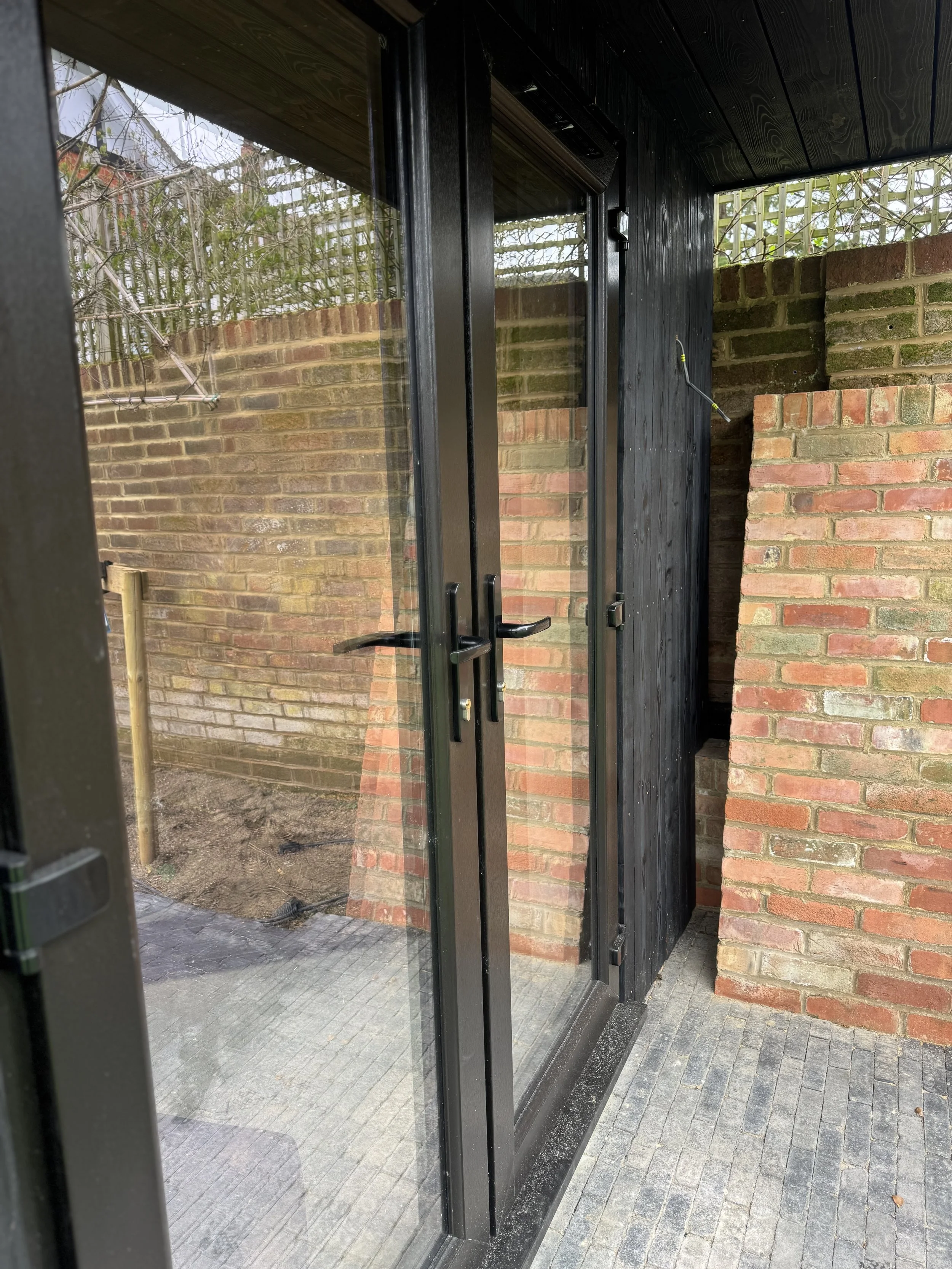 View of a black-framed glass door leading to an outdoor patio with brick walls and a wooden fence in the background.
