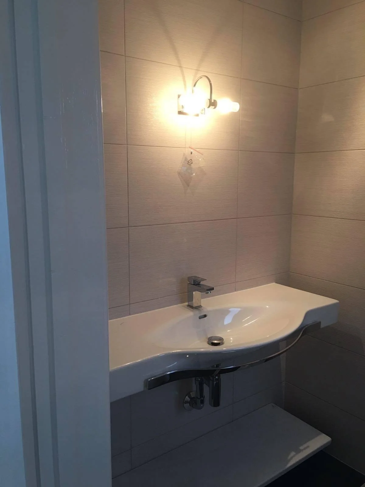 Bathroom with a wall-mounted sink, a wall light, and beige tiled walls.