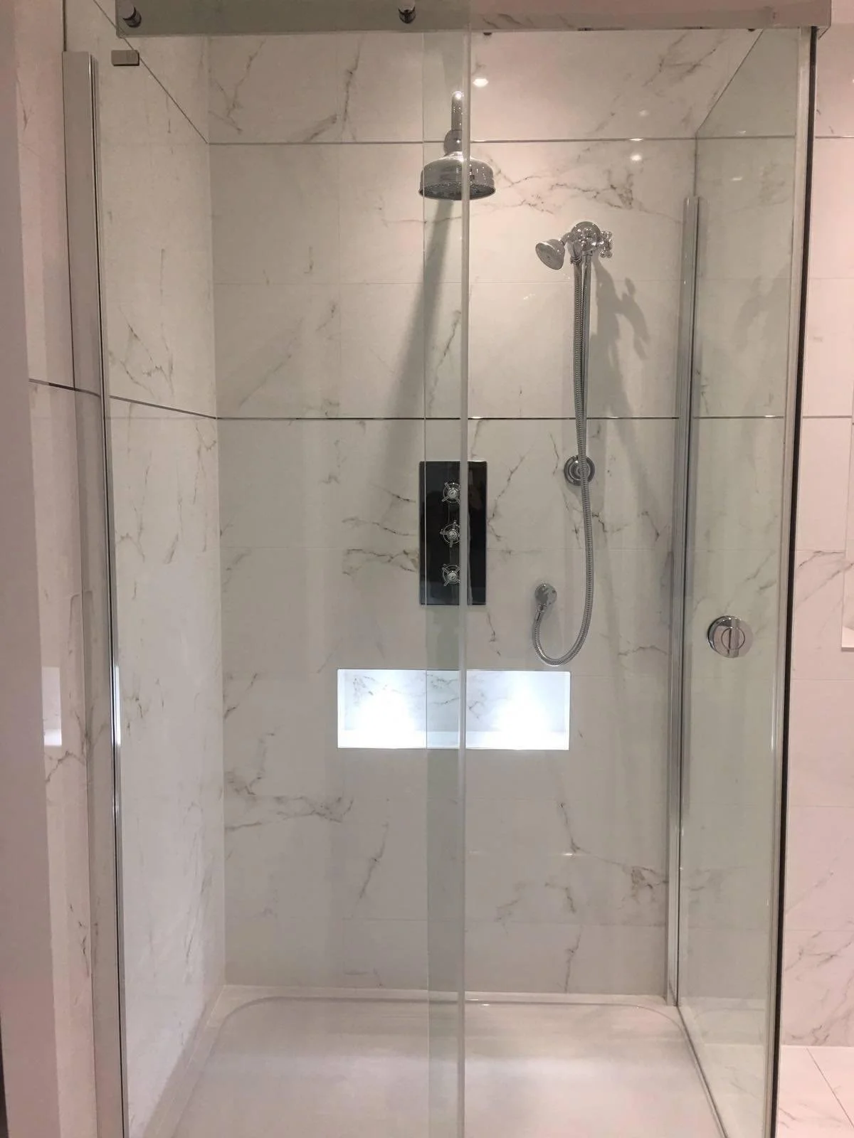 A modern shower with glass doors, marble walls, a rainfall showerhead, and a handheld showerhead.