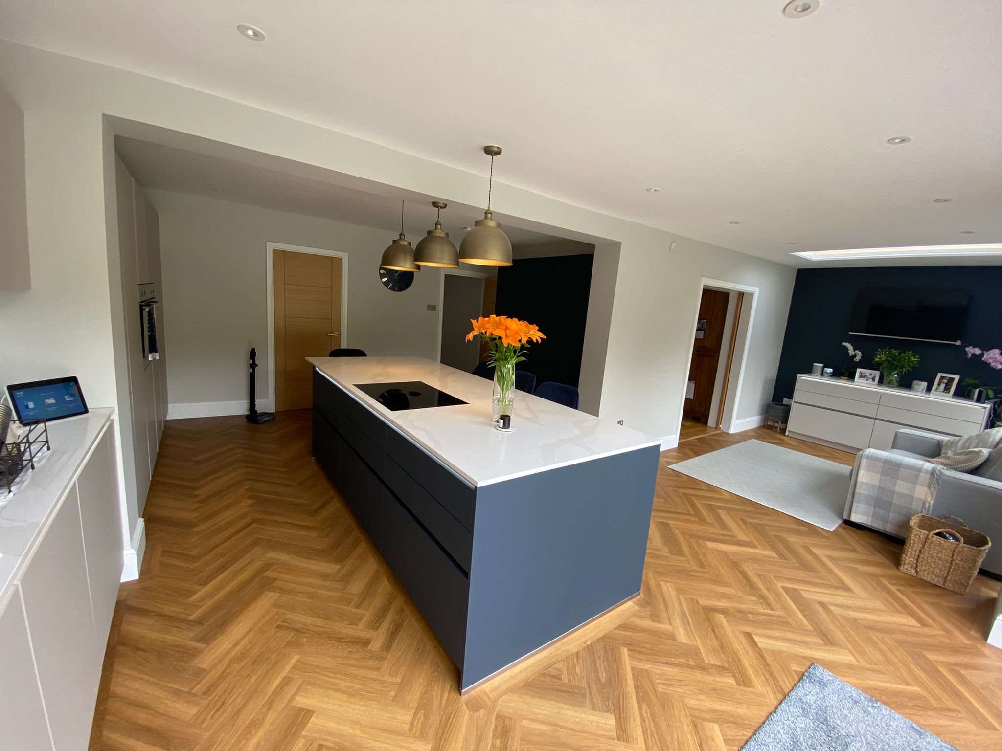 Open-concept living room and kitchen with a large white island, black cabinets, a flowery vase, and a TV on the wall.
