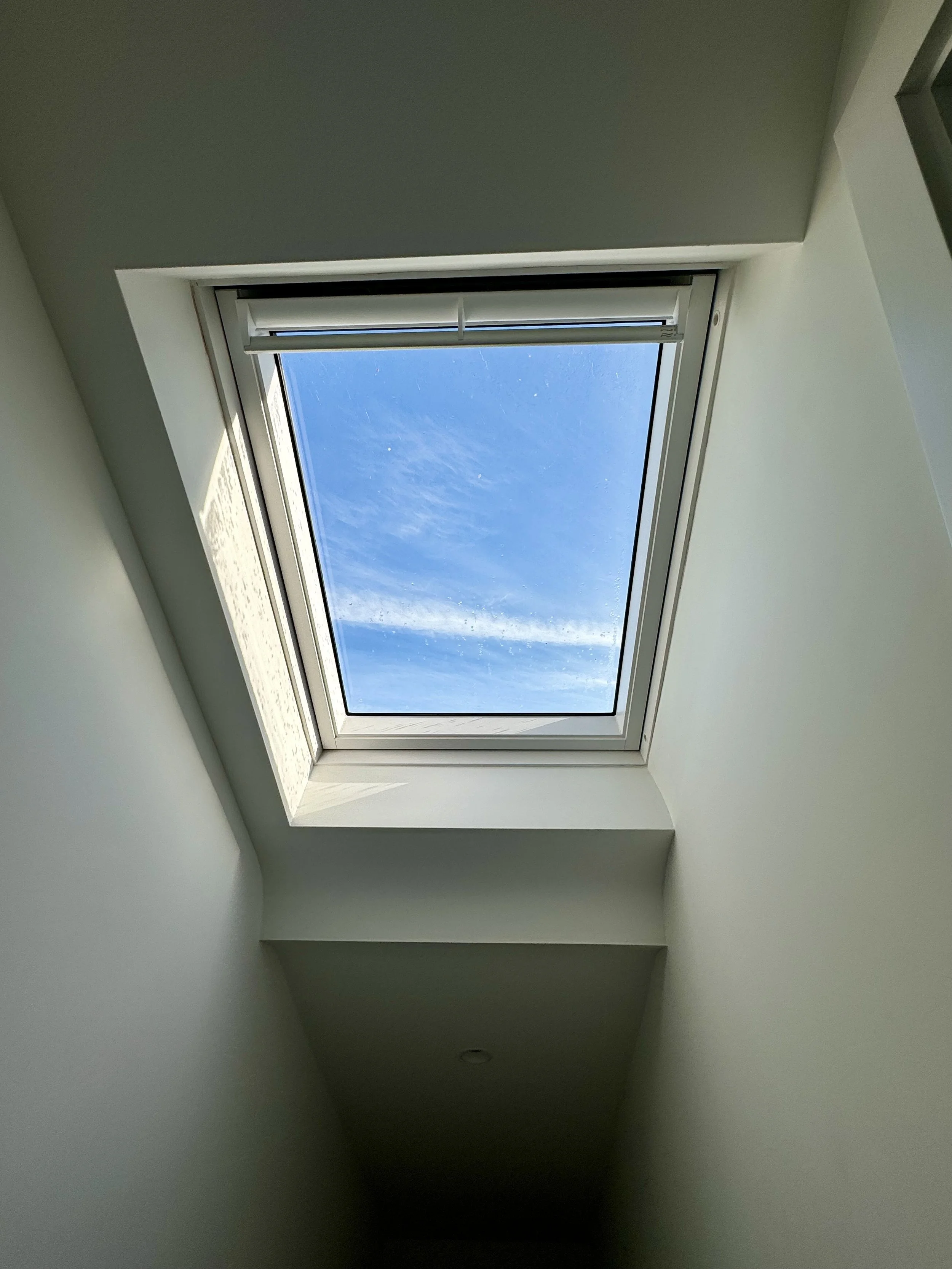 Interior ceiling towards a skylight window showing blue sky and clouds outside.