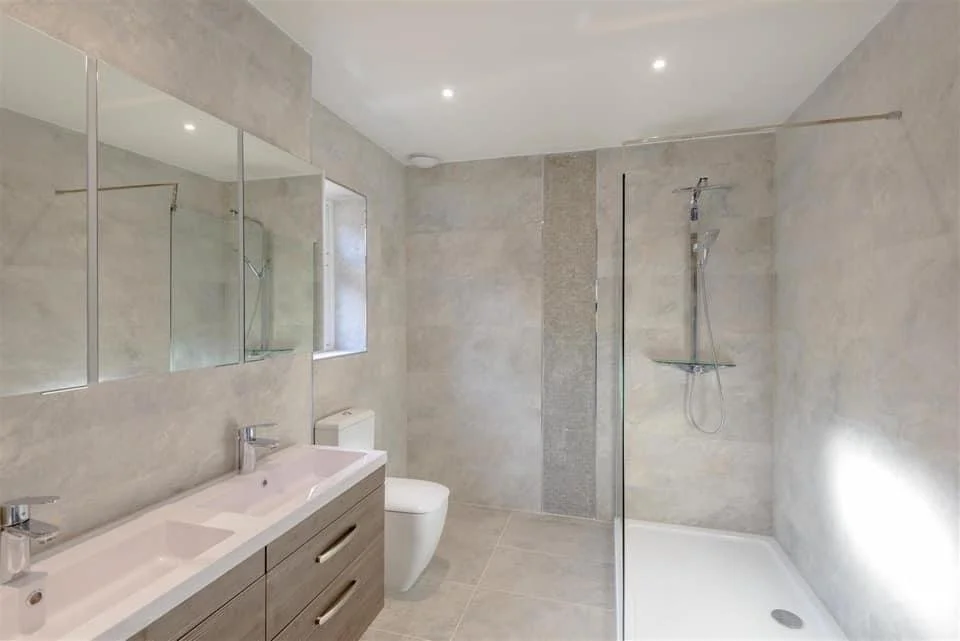 Modern bathroom with dual sinks, large mirror, toilet, and a walk-in shower with a glass partition.