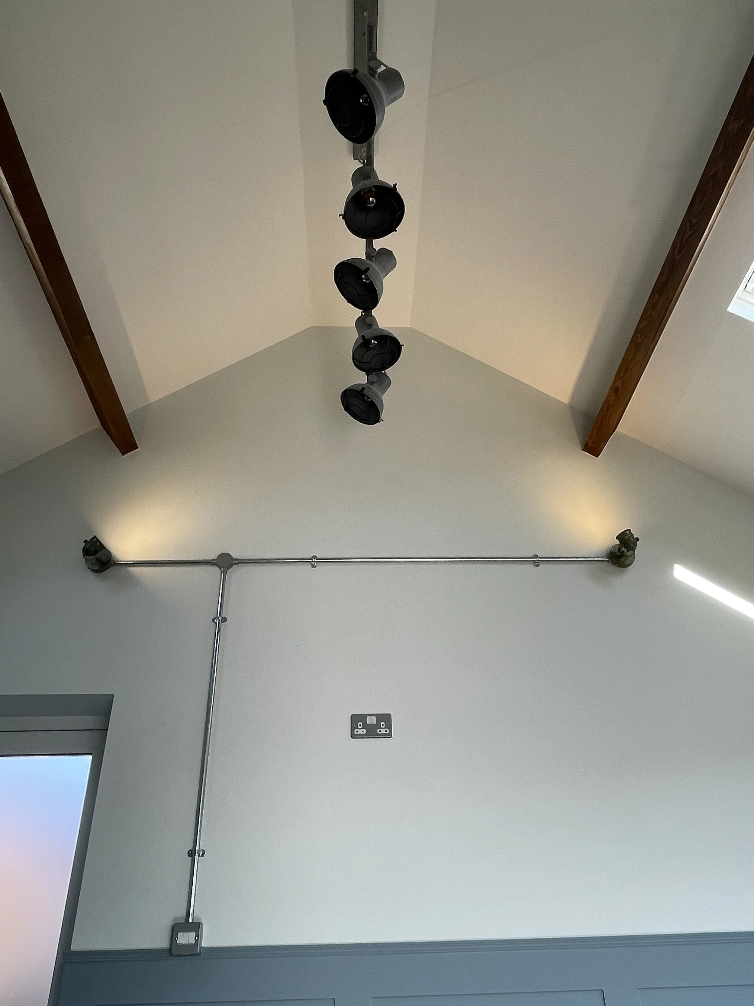 Ceiling with mounted stage lighting fixtures, electrical conduit pipes along the wall, and a ceiling outlet