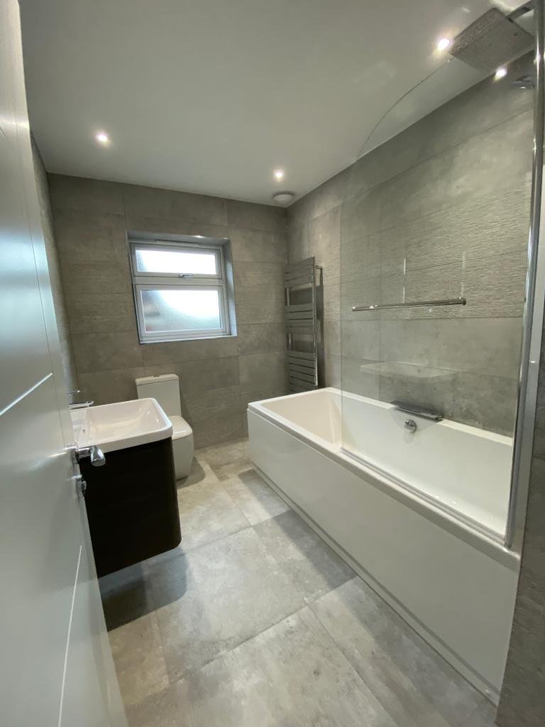 Modern bathroom with bathtub, toilet, sink vanity, gray tile walls, small window, and towel radiator.