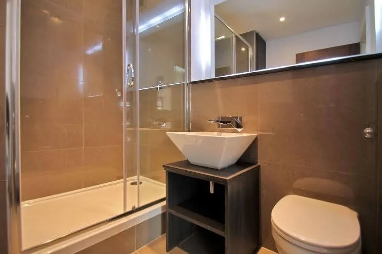Modern bathroom with a glass-enclosed shower, white vessel sink on a dark wooden vanity, and a white toilet.