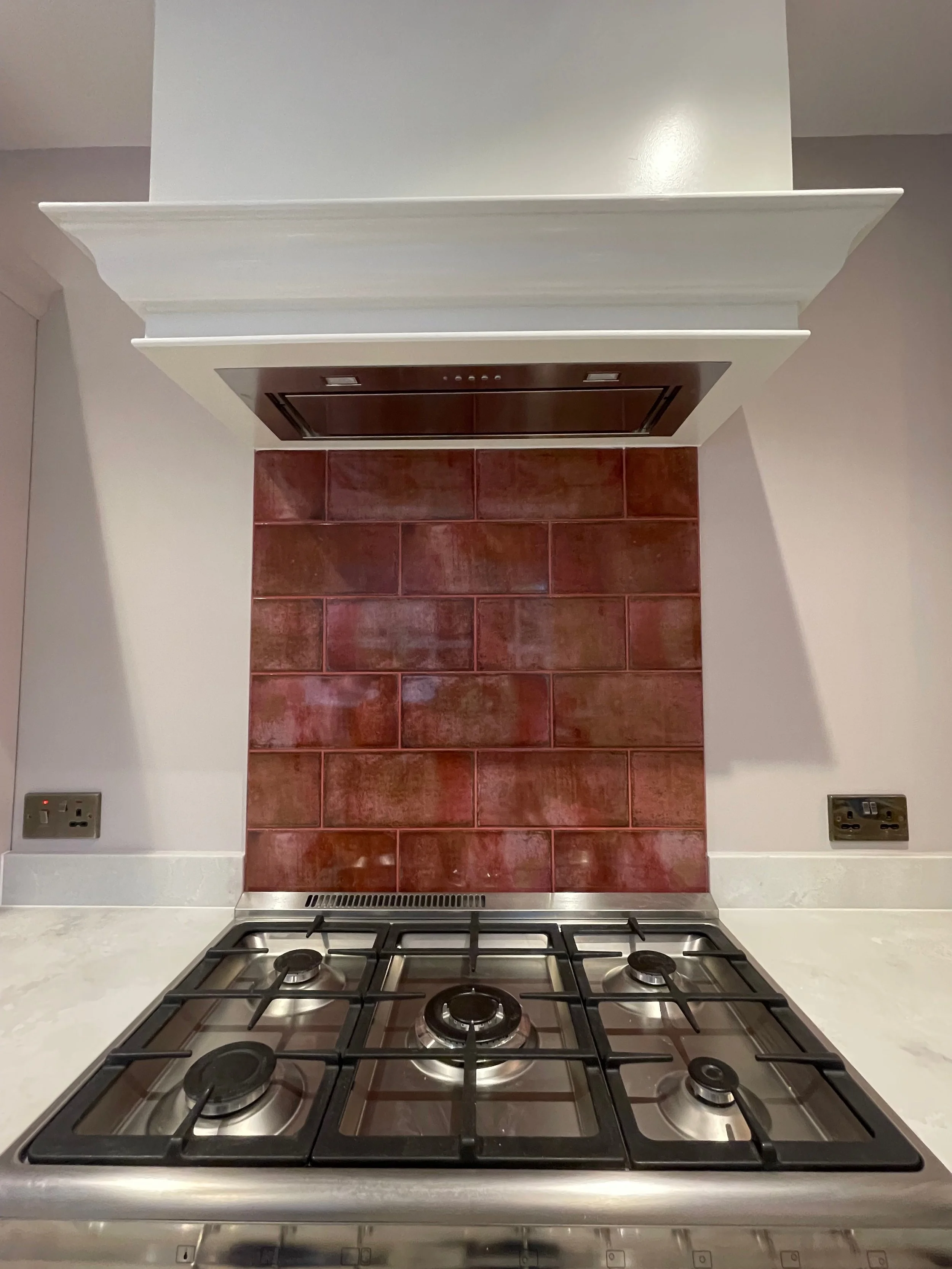 Kitchen stove with four burners, red brick backsplash, and white countertops.