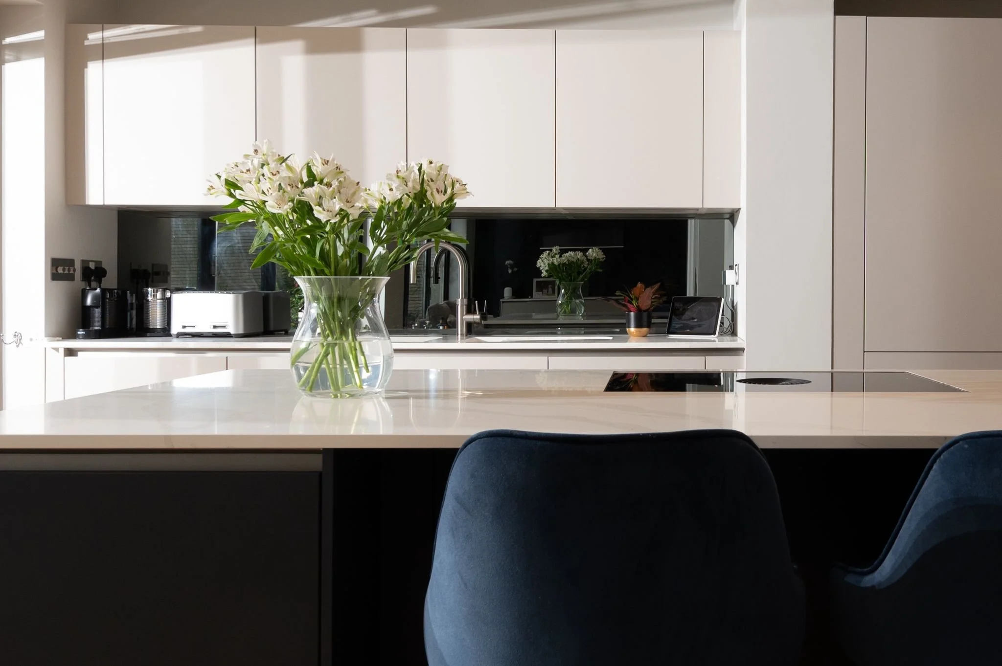 Modern kitchen with white cabinets, a white countertop, a vase of white flowers, and a dark backsplash.