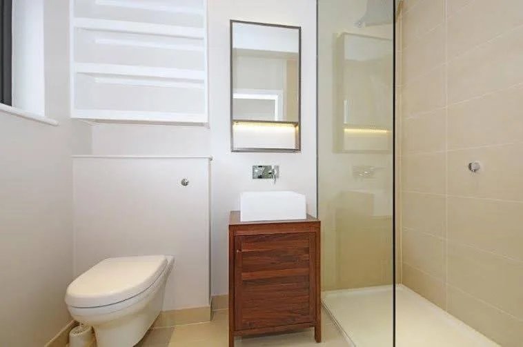 Modern bathroom with a white toilet, a wooden vanity with a vessel sink, a wall-mounted mirror, and a walk-in shower with glass partition.