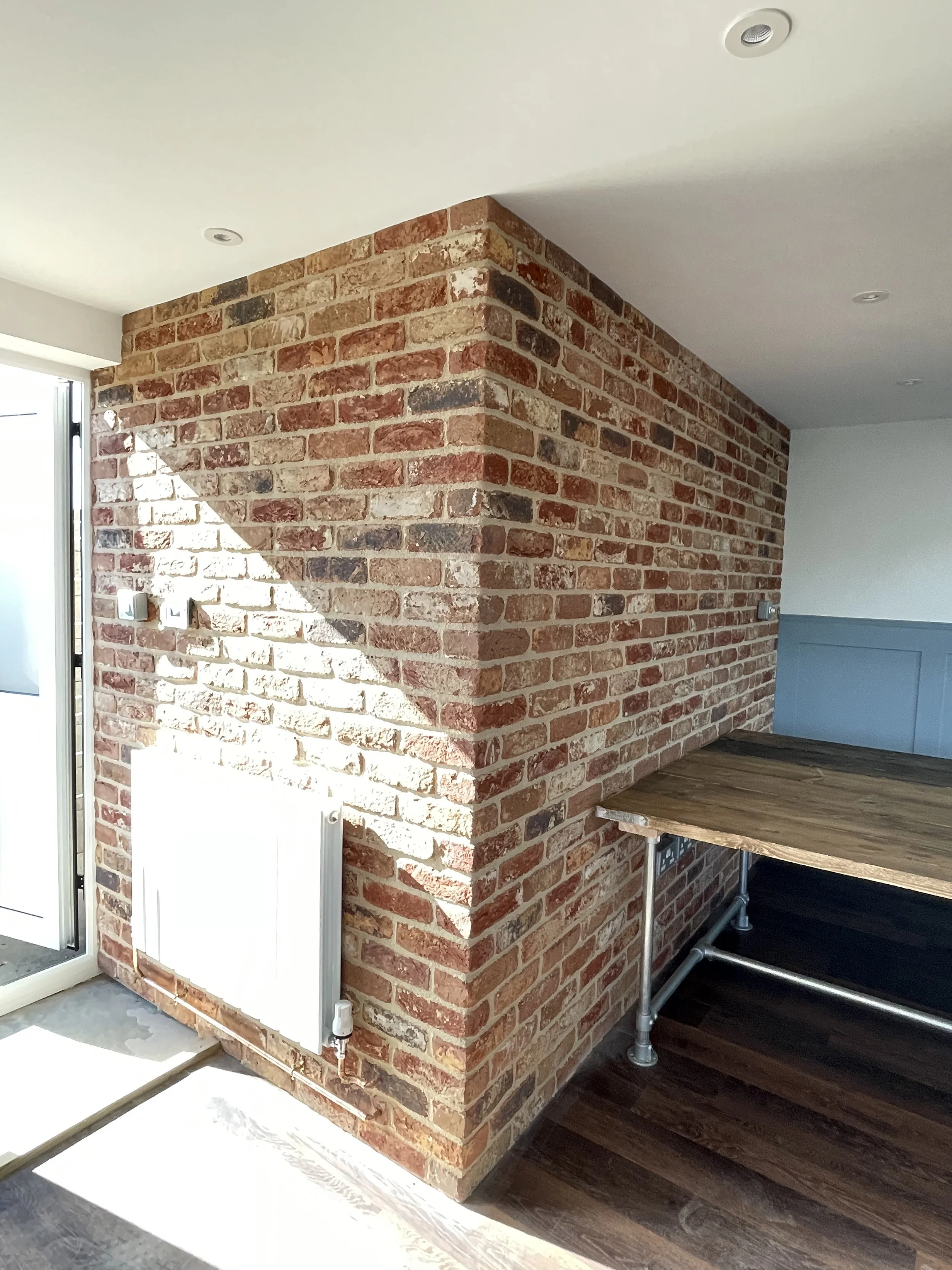 Interior corner with red brick wall, wooden floor, white ceiling, and built-in wooden counter with metal supports.