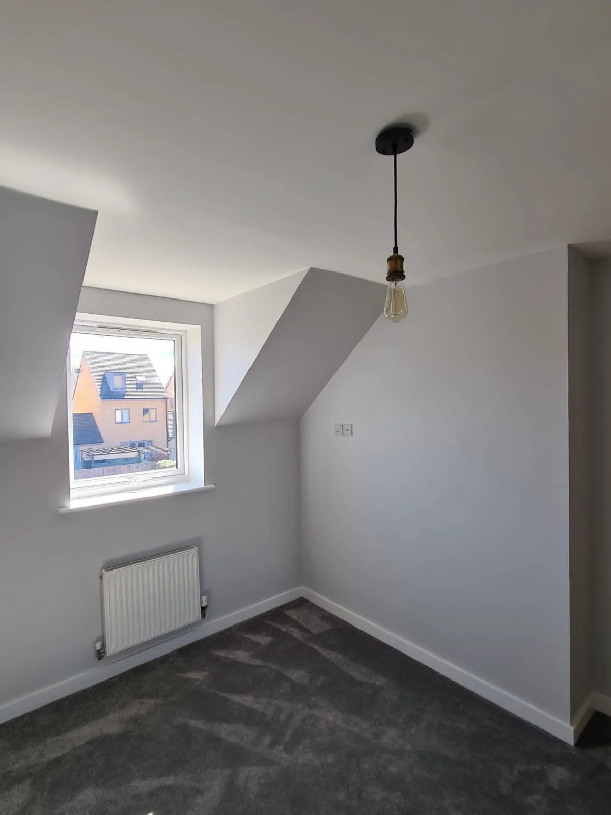 Empty room with a window, gray carpet, white walls, and a ceiling light fixture without a cover.