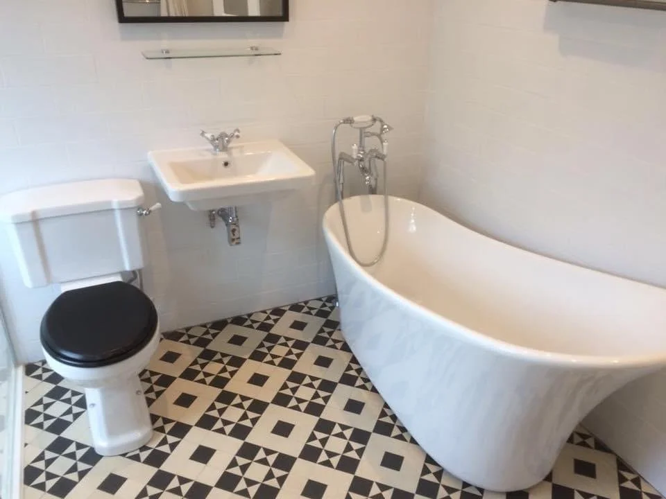 Bathroom with a vintage white clawfoot bathtub, a small wall-mounted sink, a toilet with a black seat, and black and white geometric patterned tile floor.
